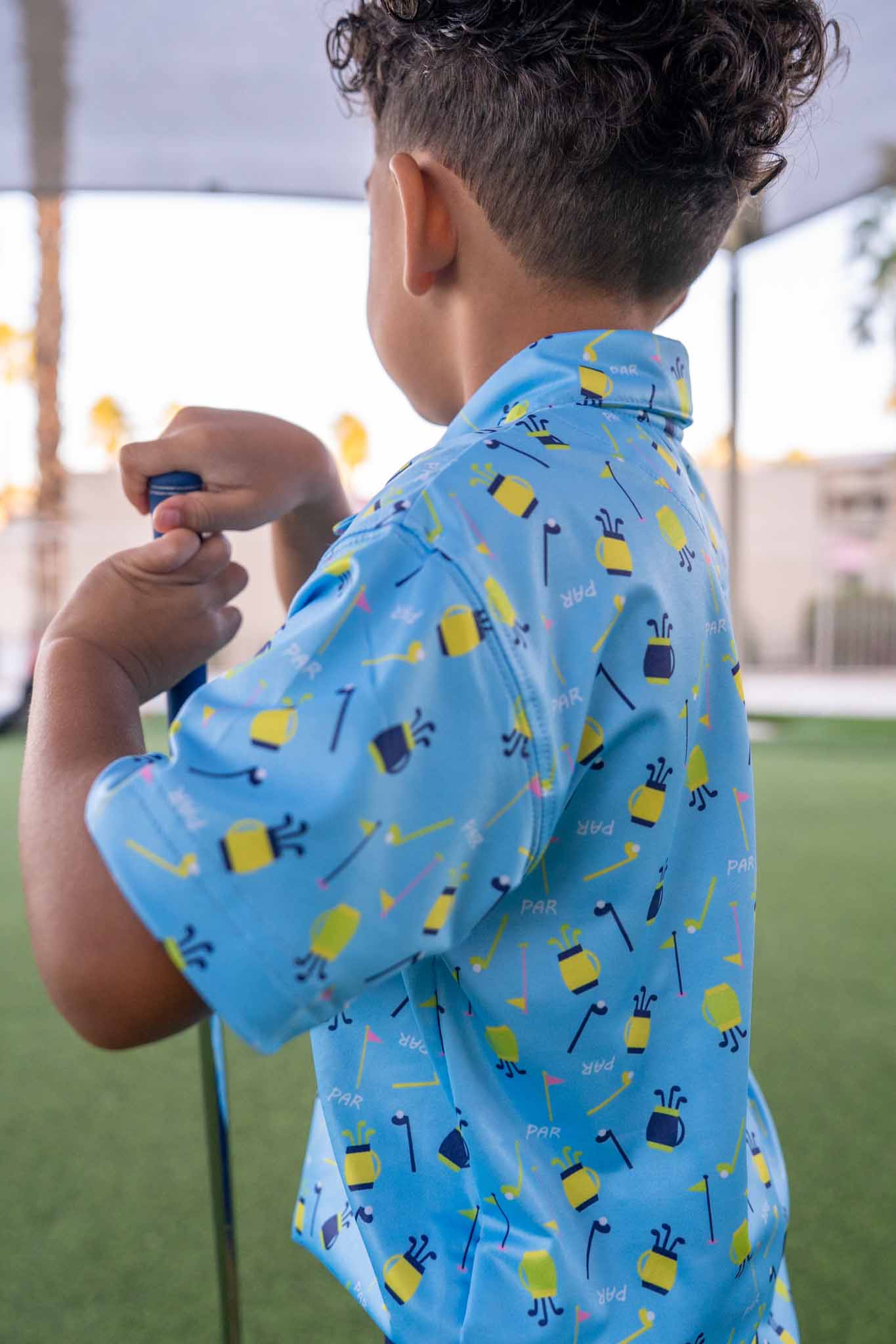 Child wearing a blue shirt with golf-themed pattern outdoors