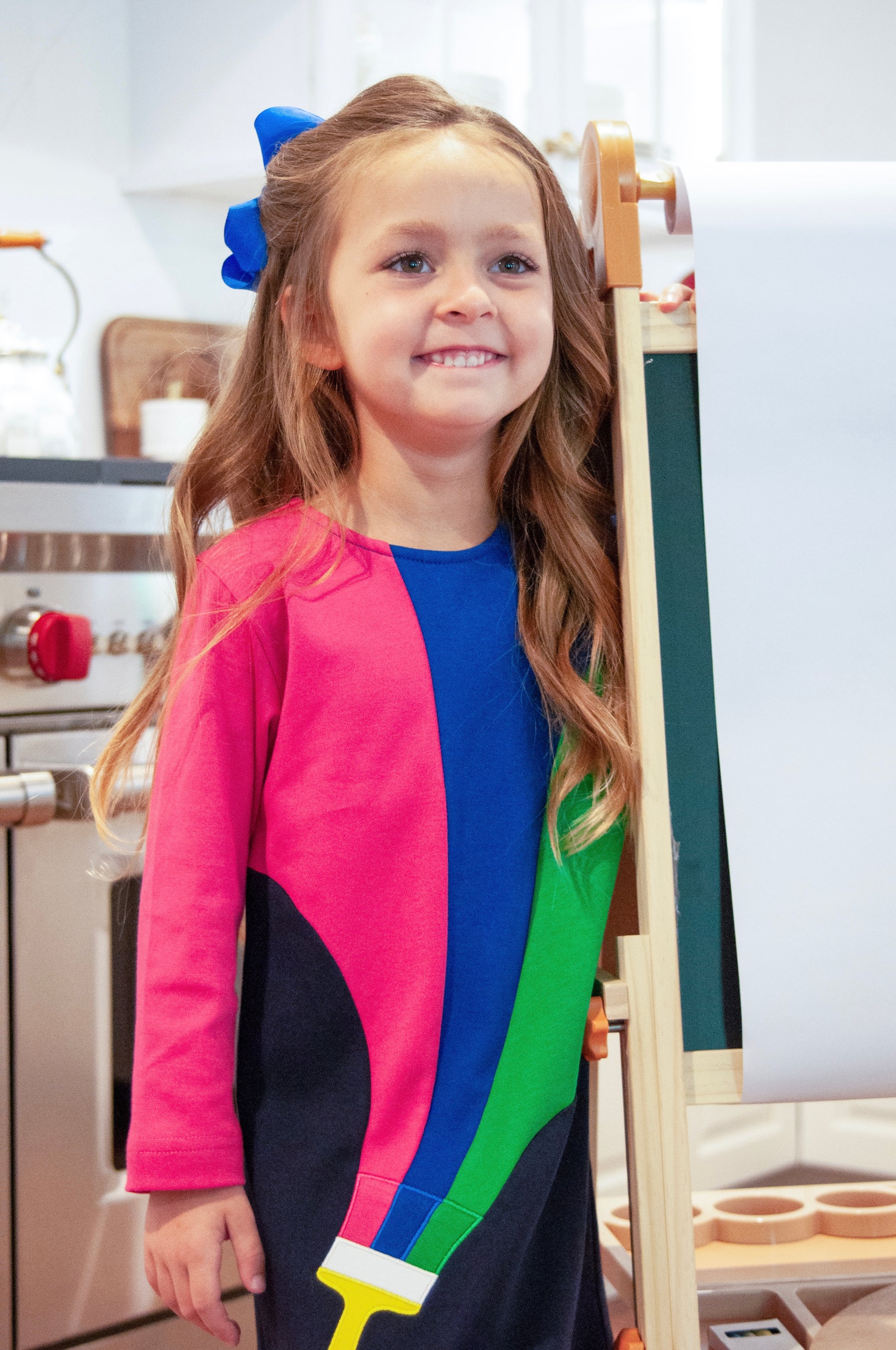 Young girl in a colorful dress standing in a kitchen.