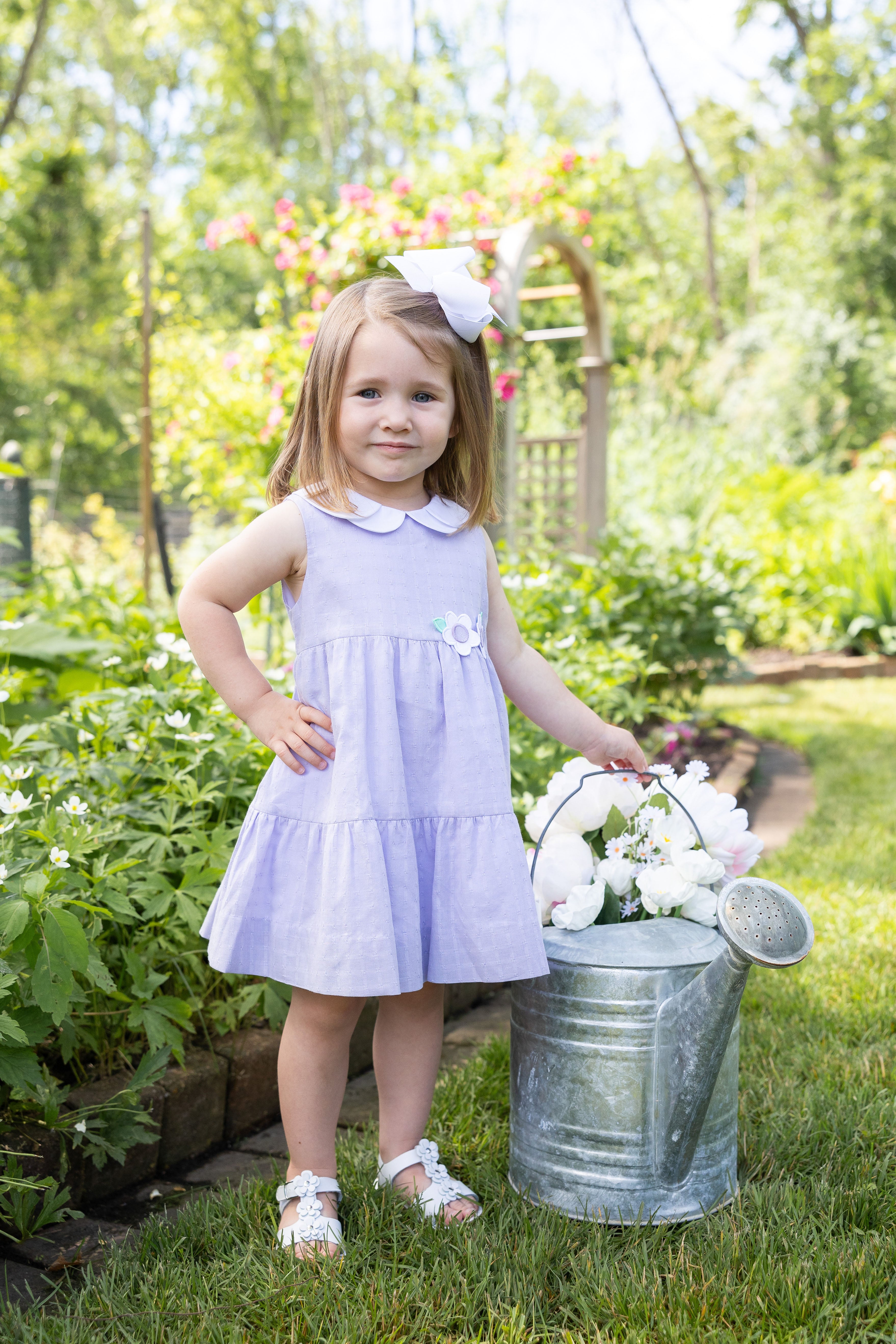 young girl in garden wearing lavender dress with collar and flower appliques