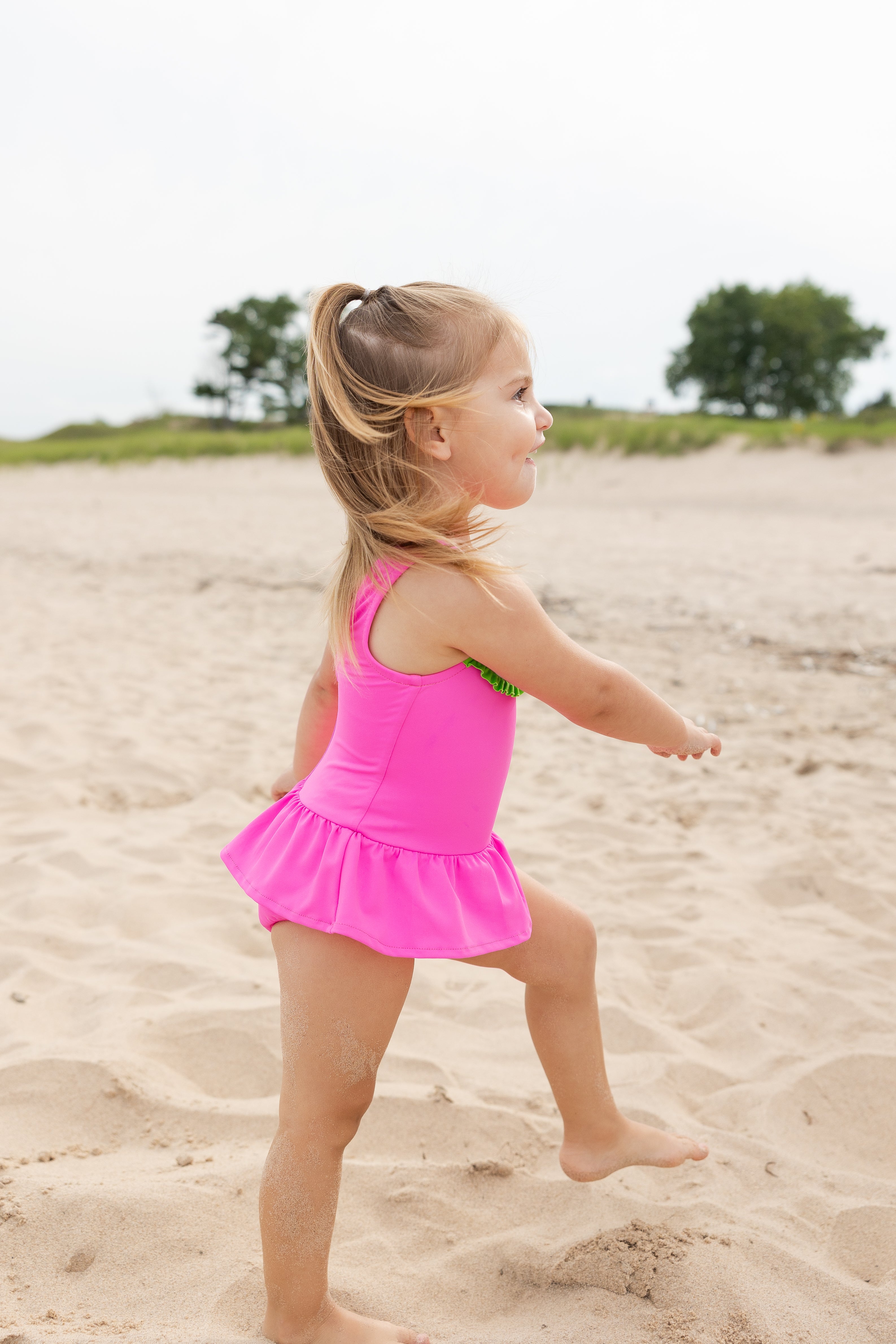 young girl on beach in pink watermelon swimsuit