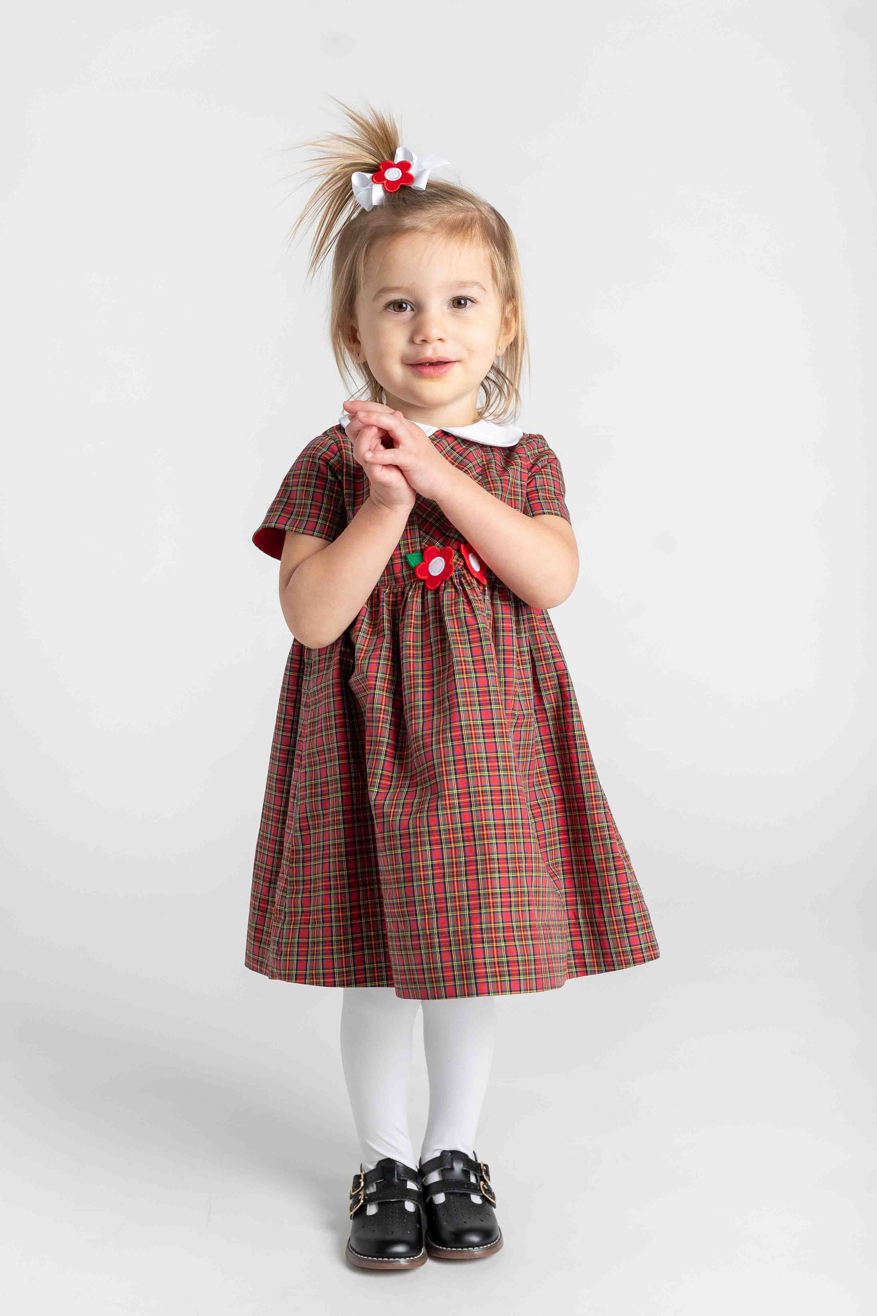 Young girl wearing a red plaid dress with a white collar on a white background