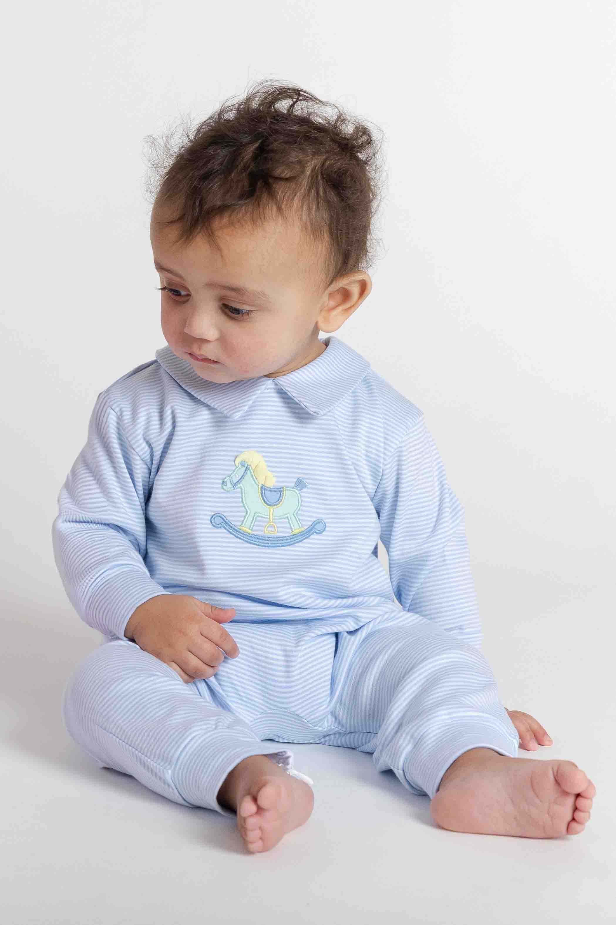 Baby wearing a light blue outfit with a rocking horse design on a white background