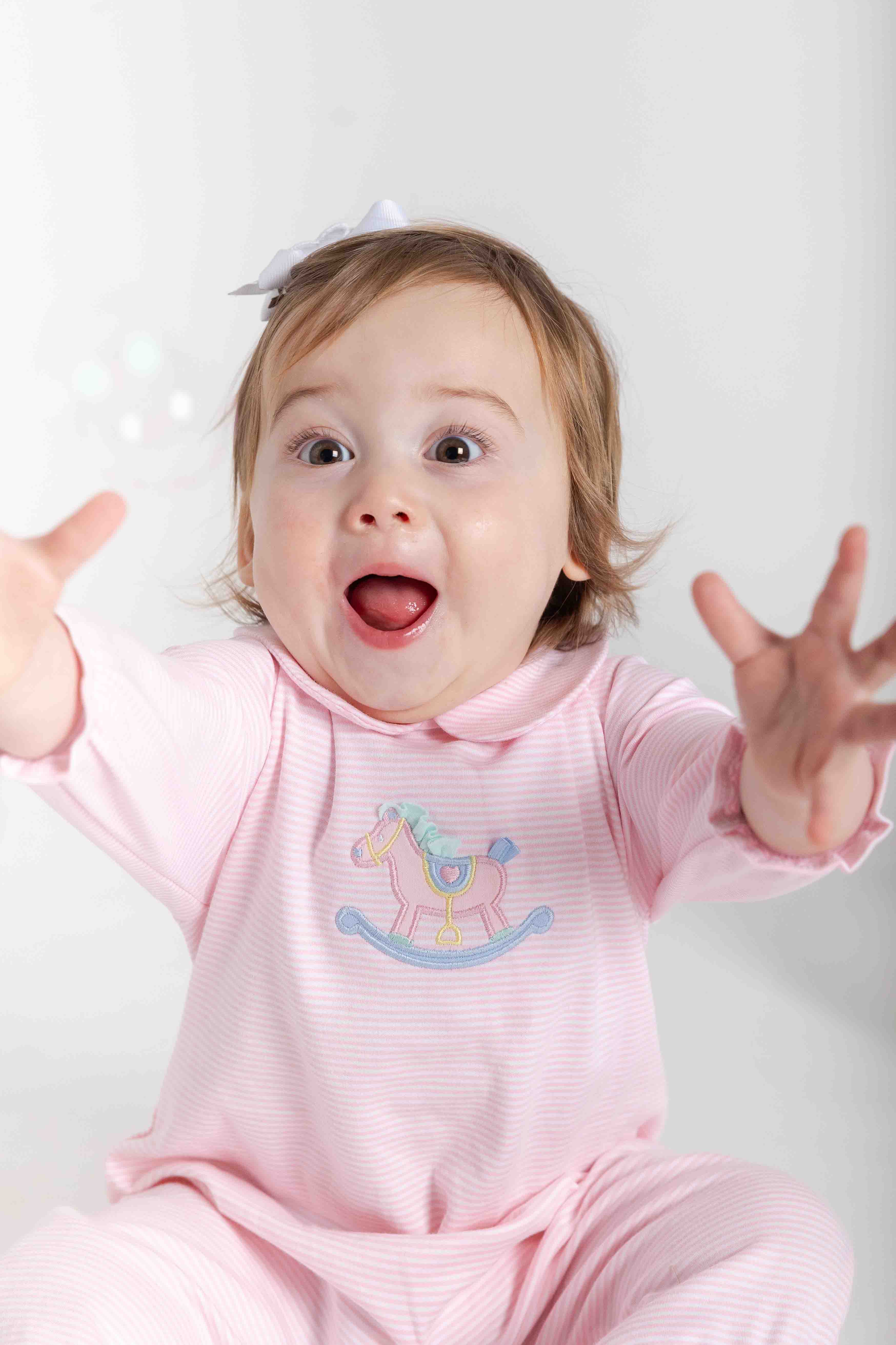 Baby in a pink outfit with a rocking horse design on a white background