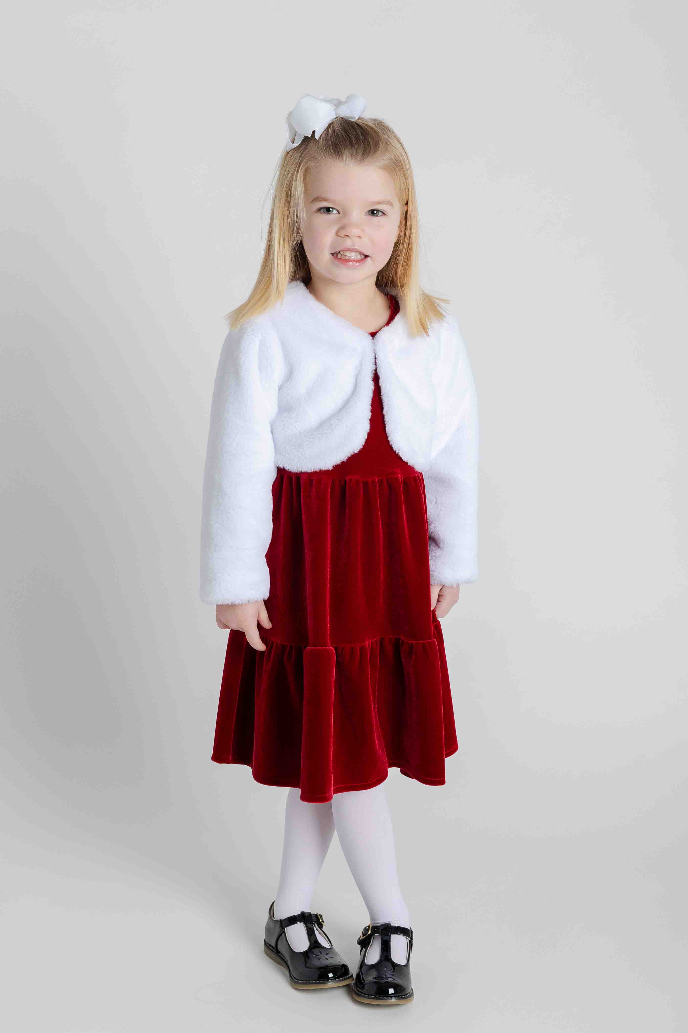 Young girl wearing a white cardigan and red dress on a plain background