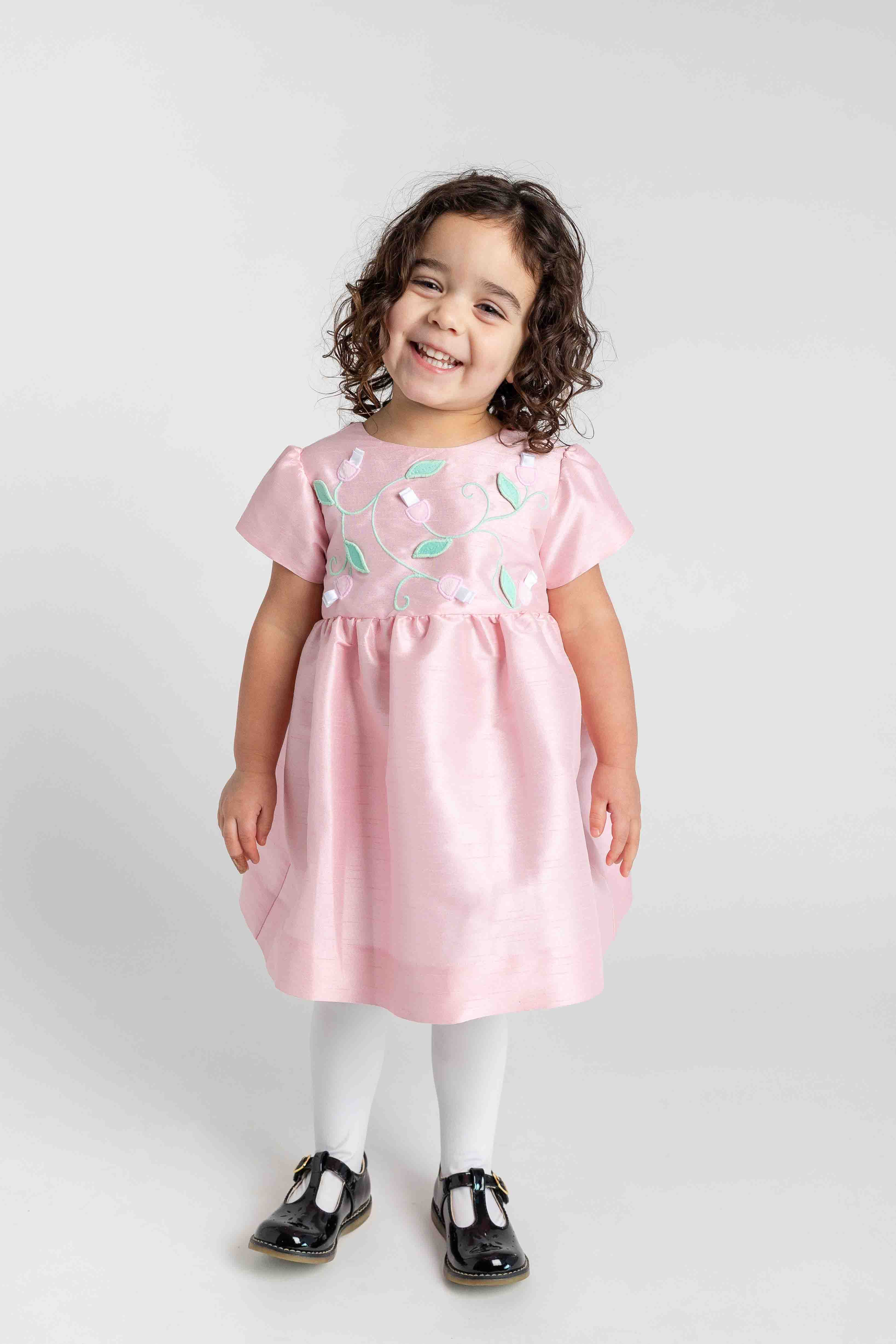 Child wearing a pink dress with heart patterns on a white background