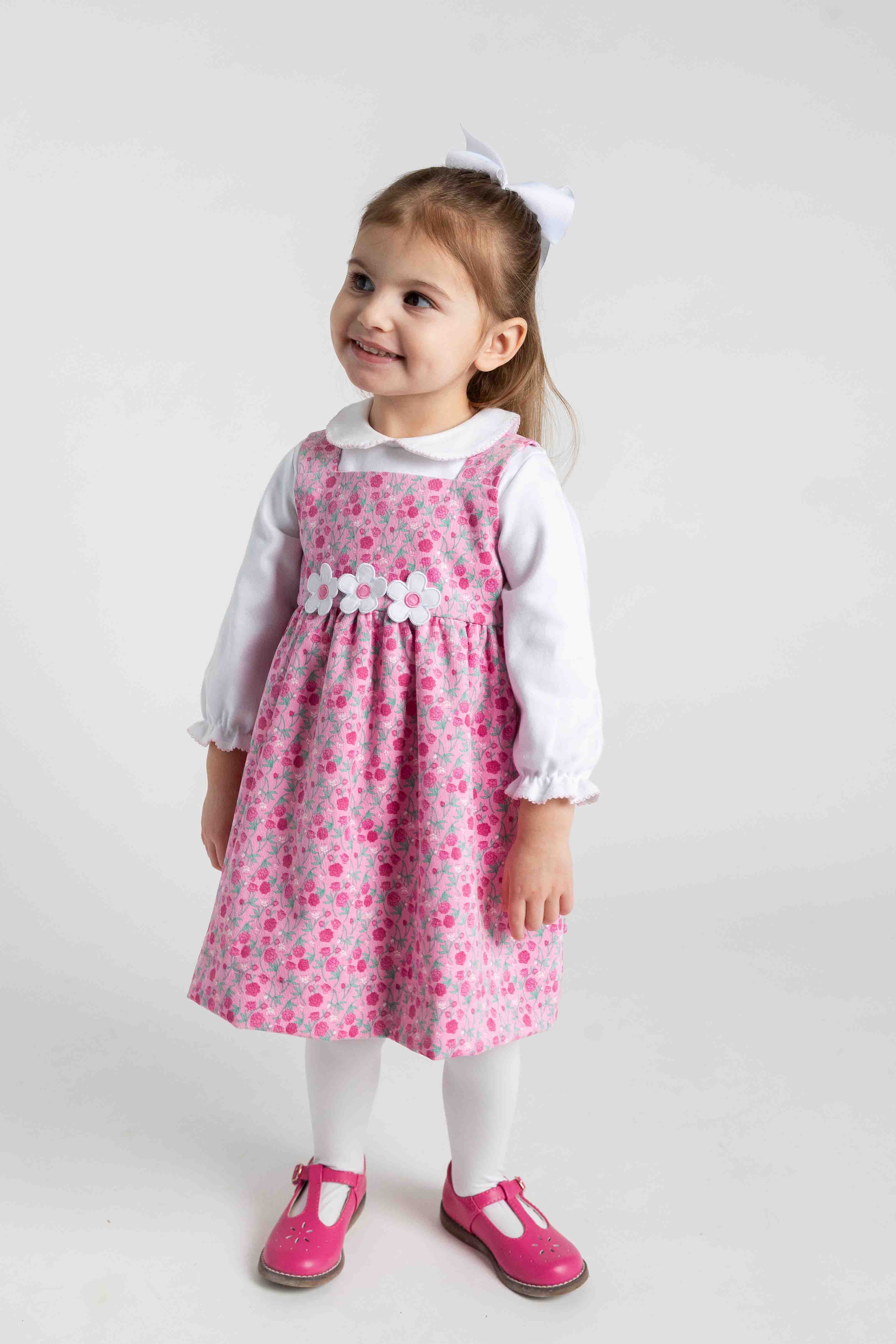 Young girl wearing a pink floral dress with a white shirt underneath on a light gray background