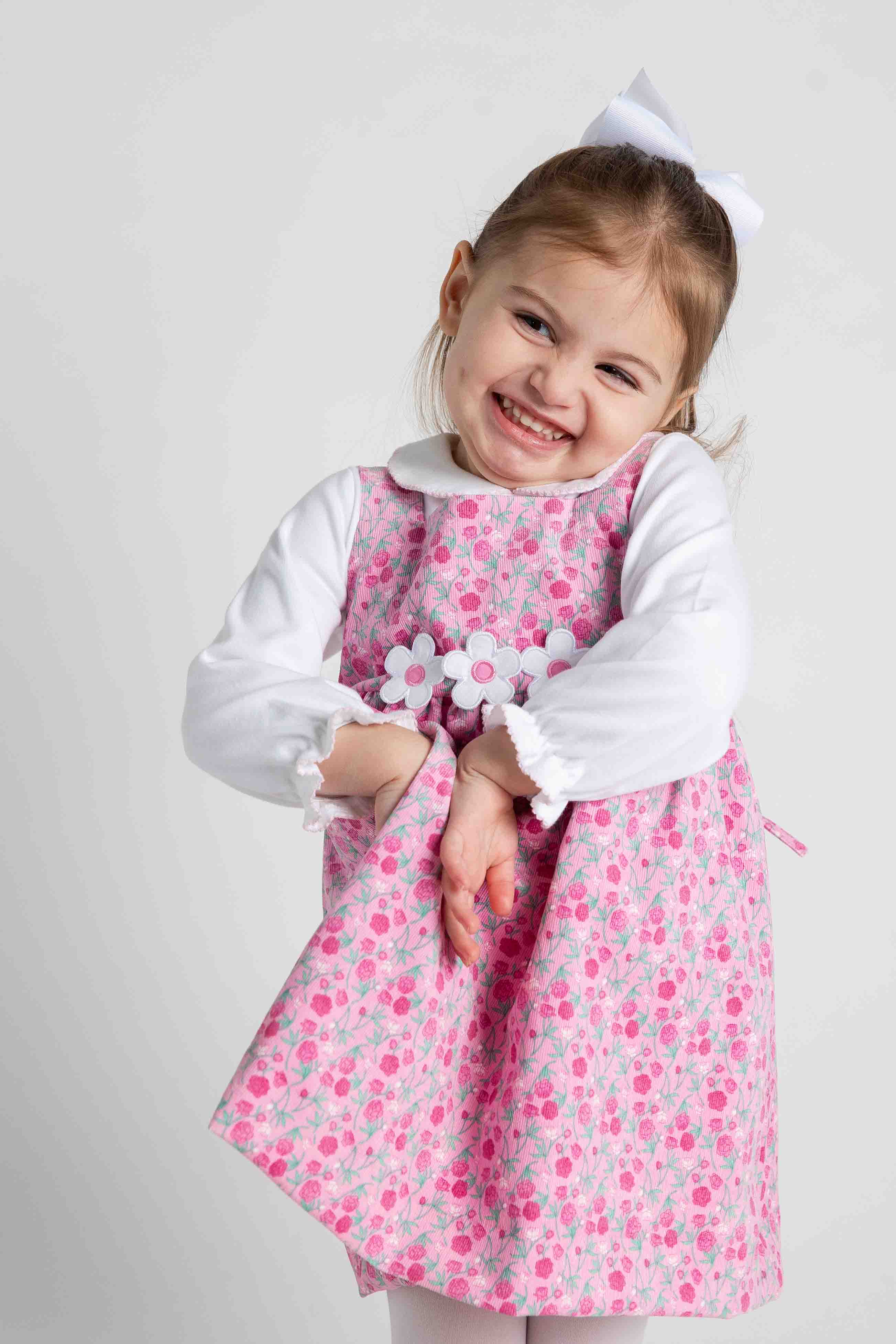 Young girl wearing a pink floral dress with a white shirt underneath on a light gray background