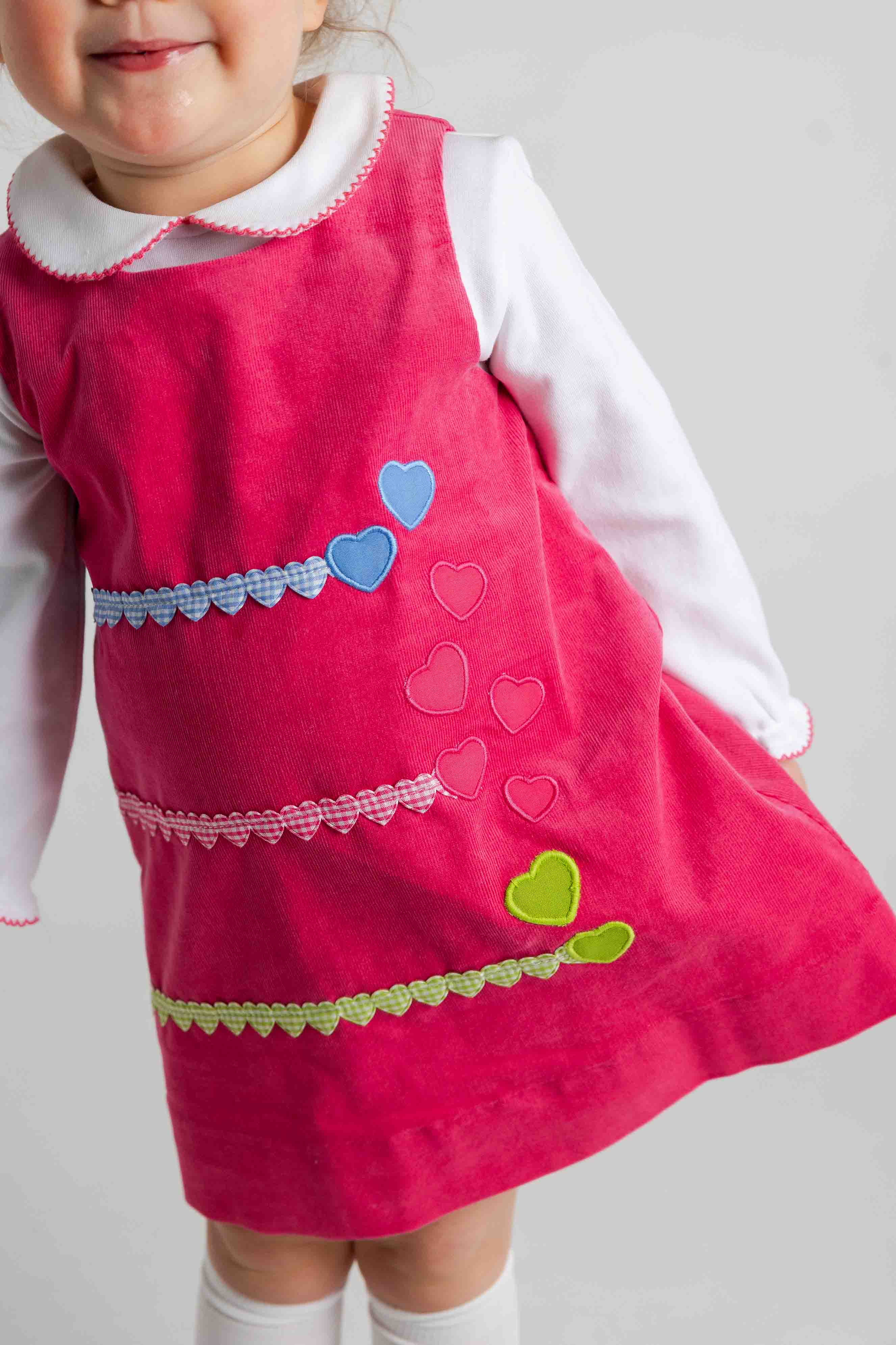 Child wearing a pink dress with heart patterns on a plain background