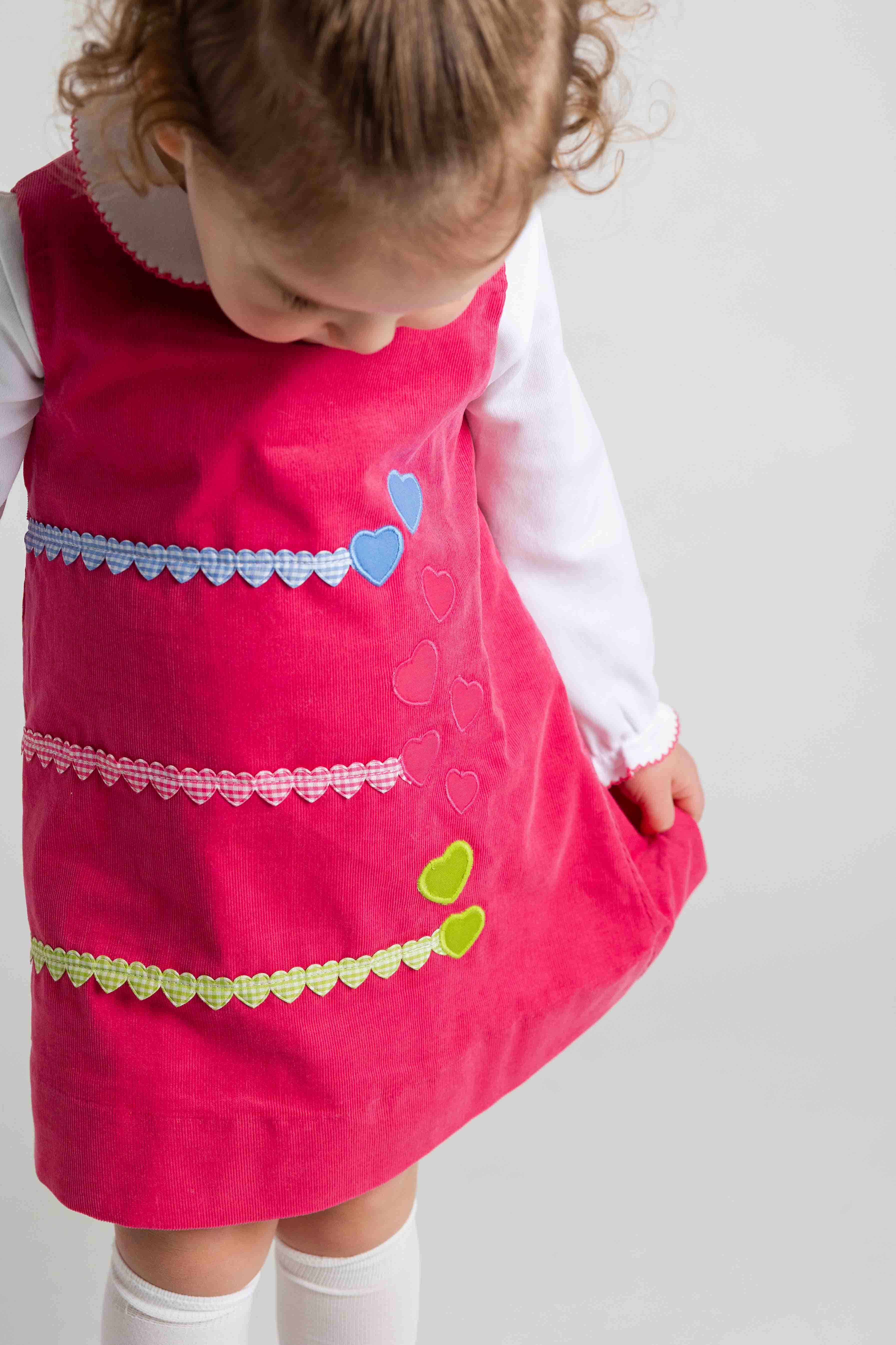 Child wearing a pink dress with colorful heart patterns on a white background
