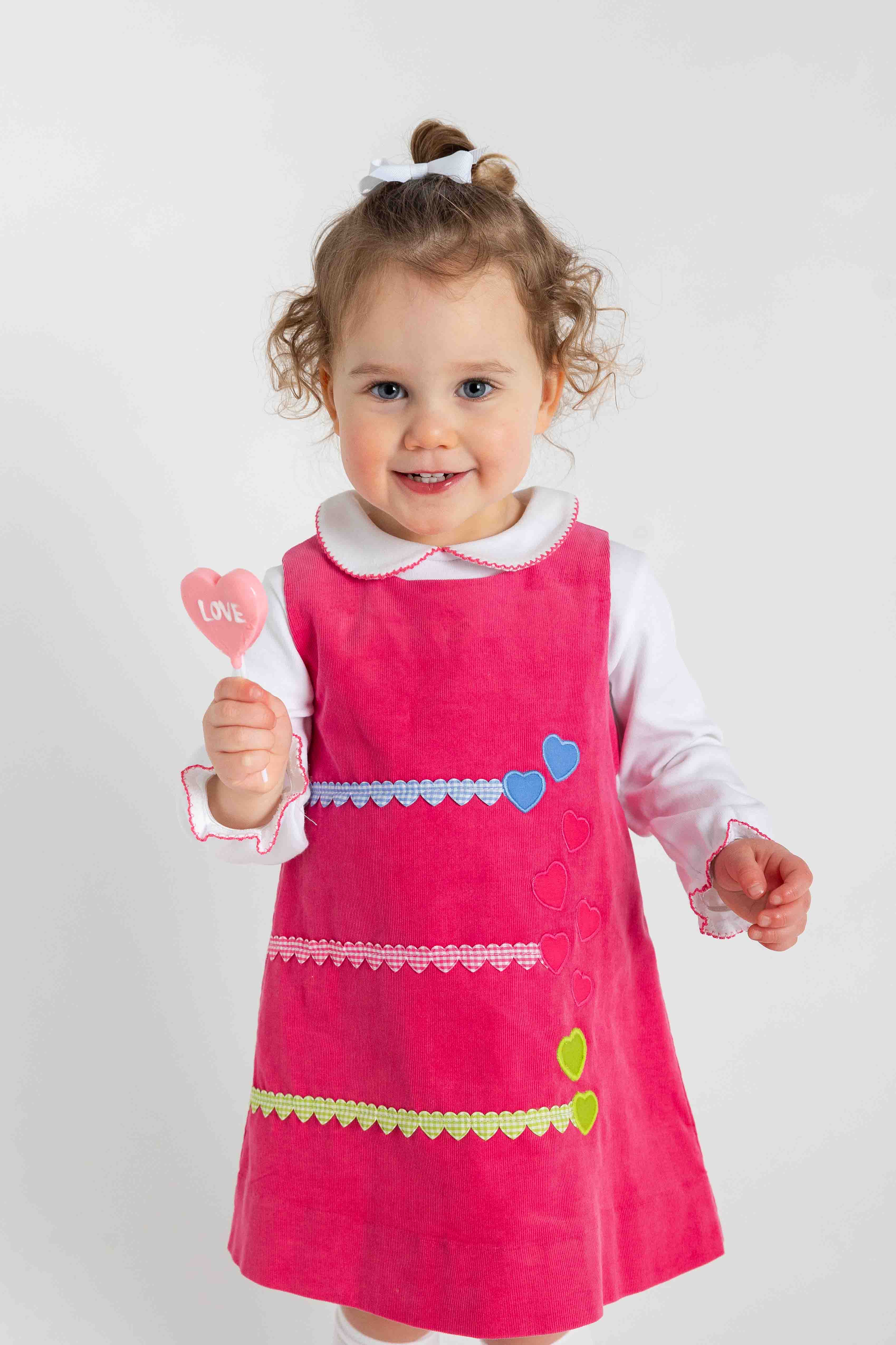 Child wearing a pink dress with heart patterns on a white background