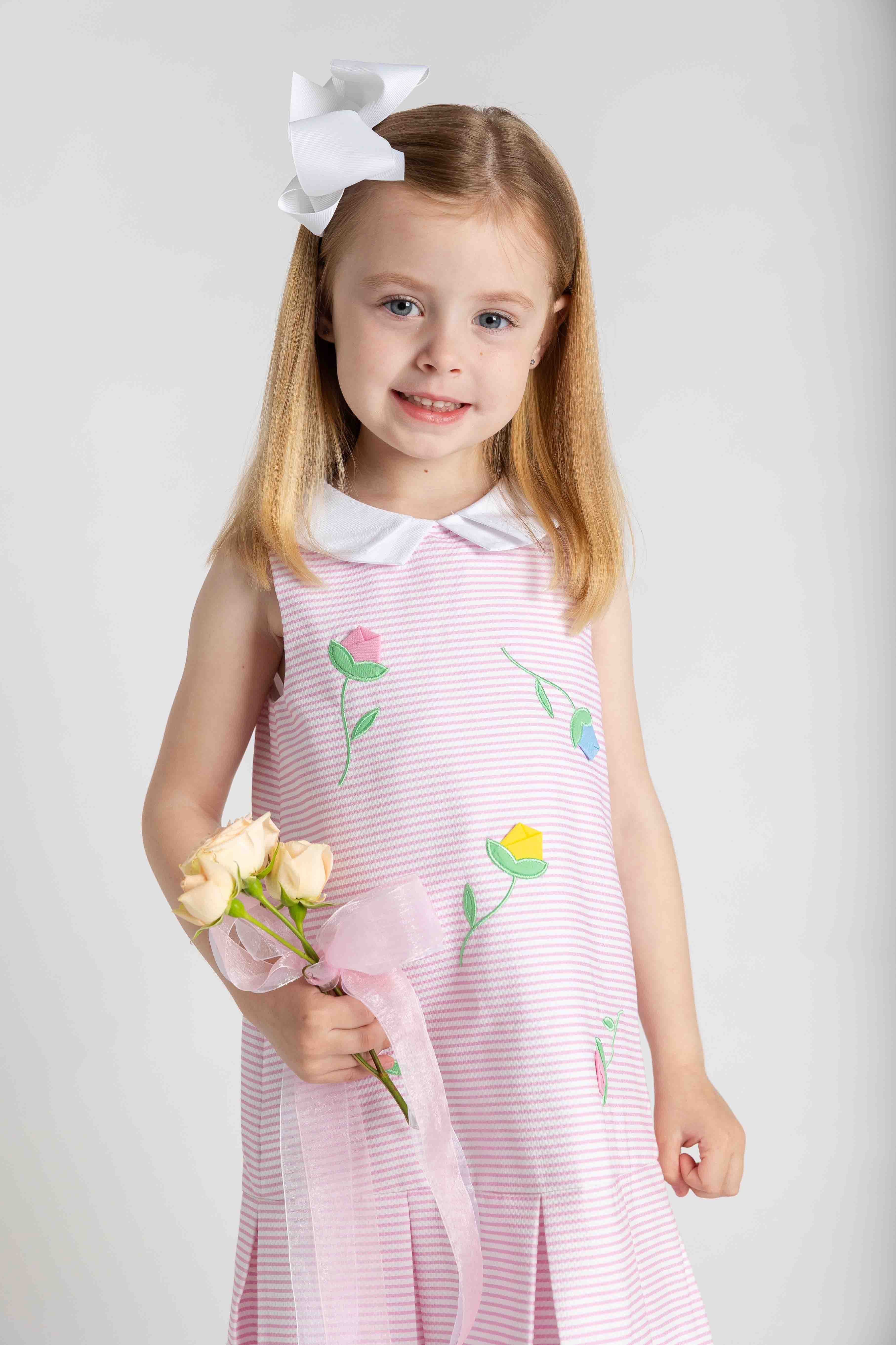 Young girl in a pink dress with floral designs holding flowers against a white background