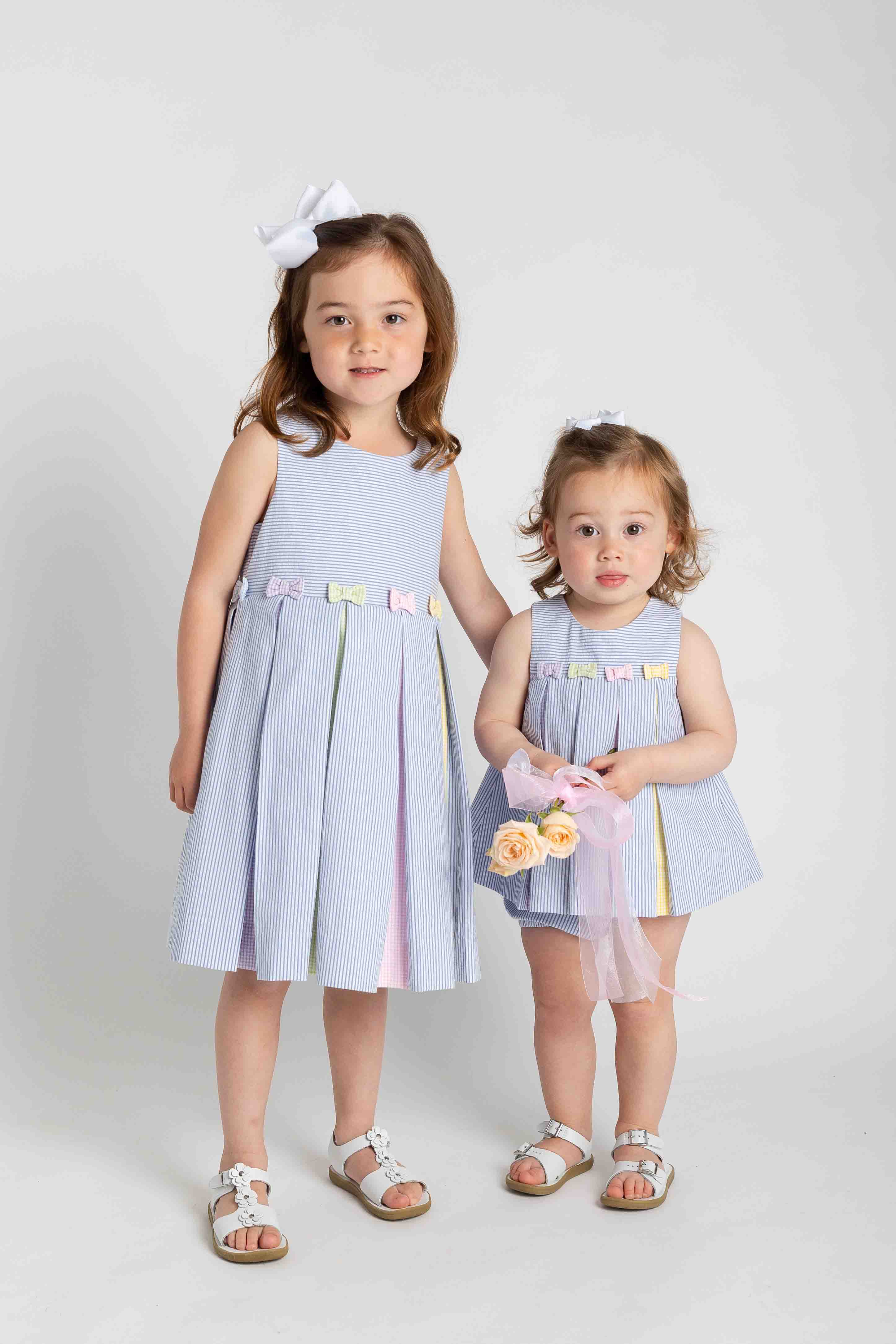 Two young girls wearing matching light blue dresses with colorful accents on a white background.