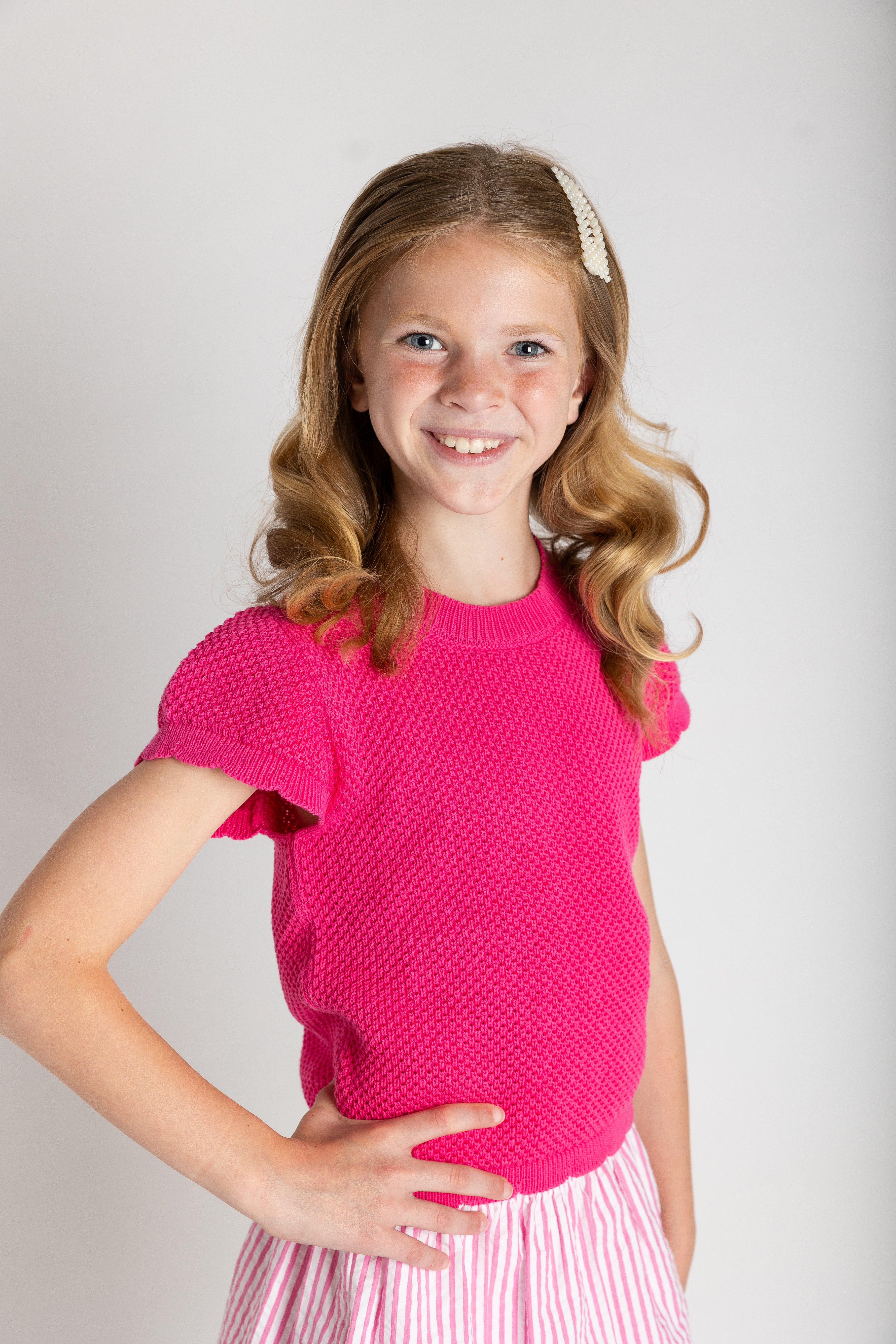 Young girl wearing a pink knitted top and striped skirt on a plain background
