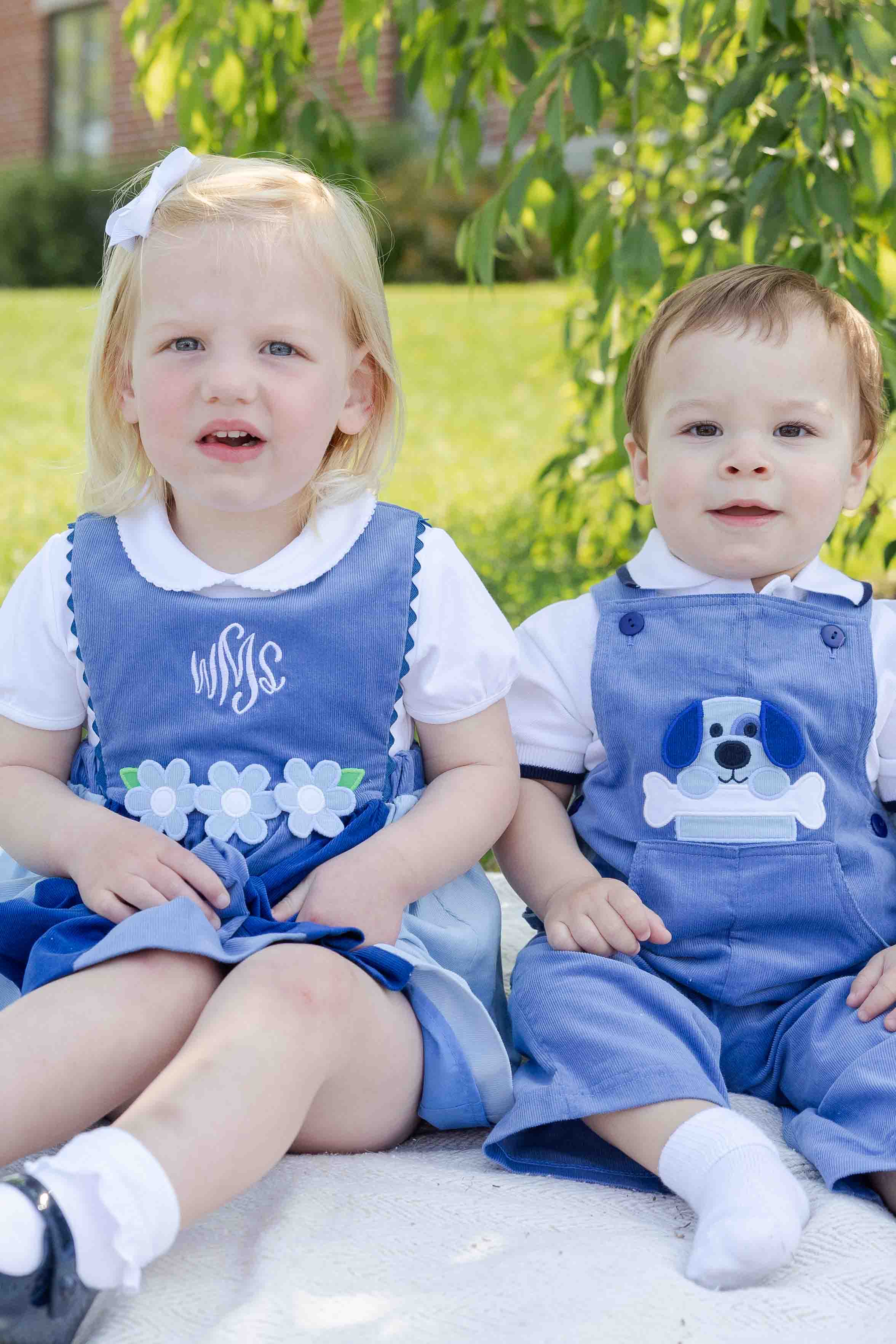 Two children in matching blue outfits sitting outdoors.