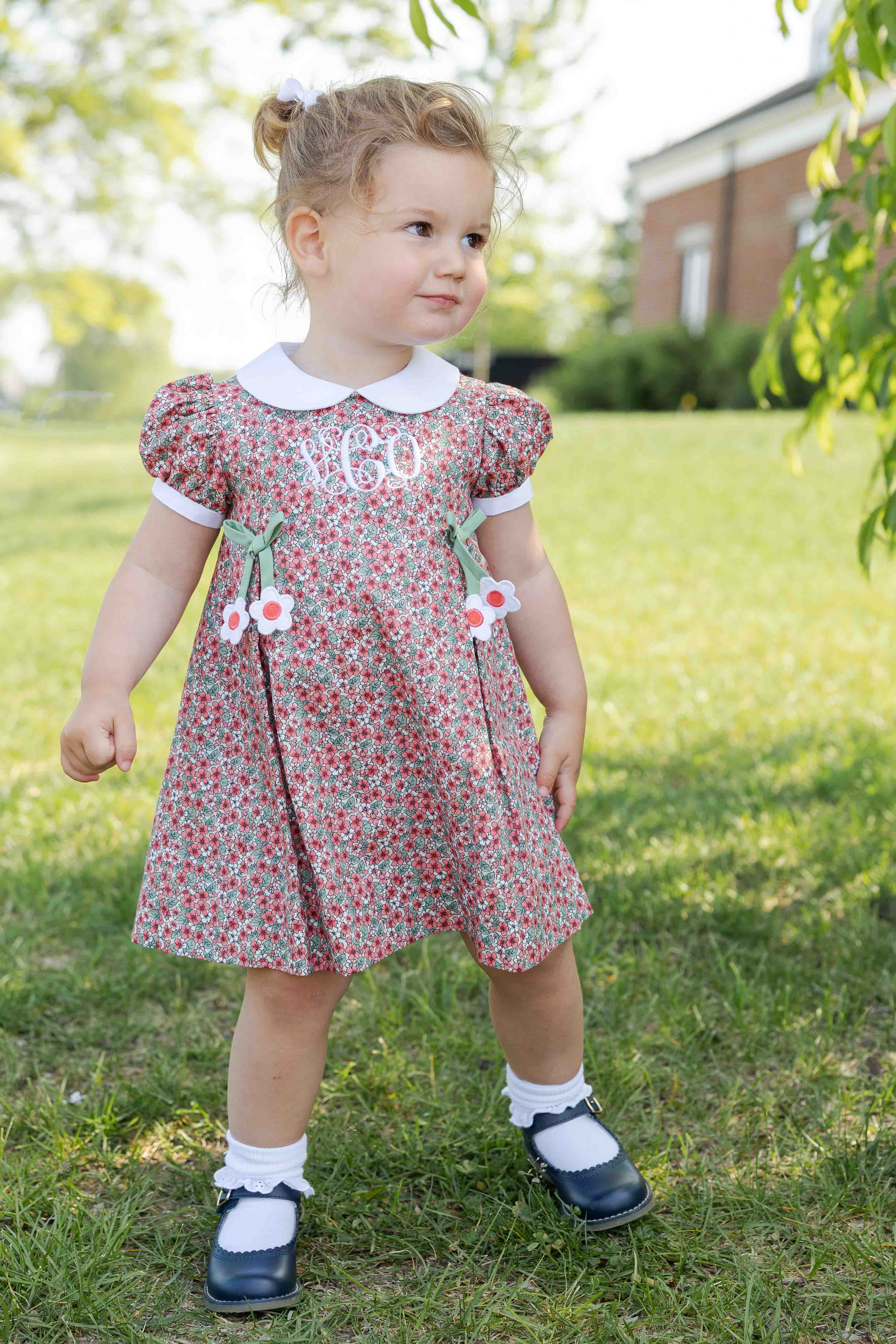 Young girl in a floral dress standing on grass with a building in the background