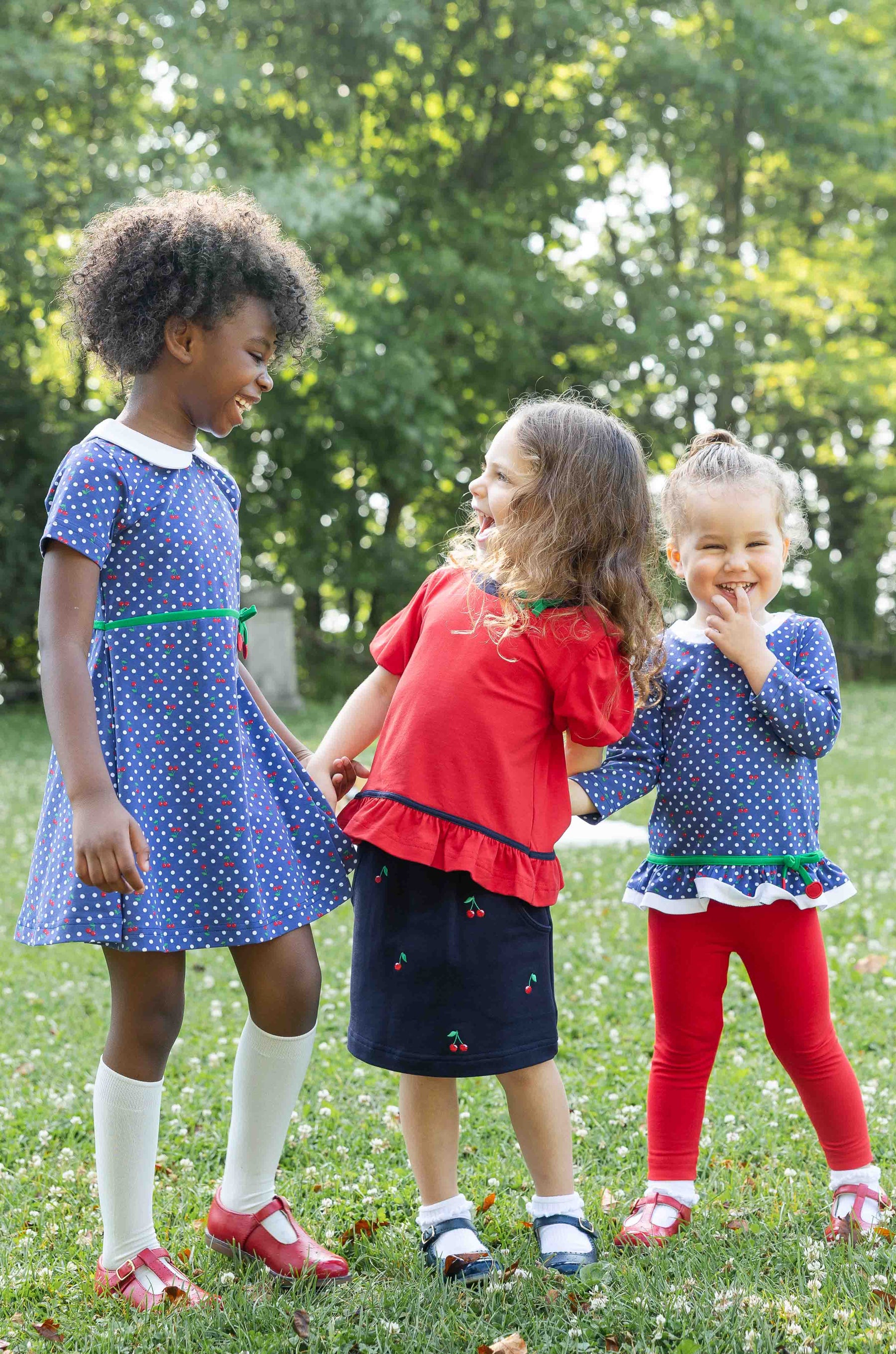 Three children standing in a grassy area with trees in the background