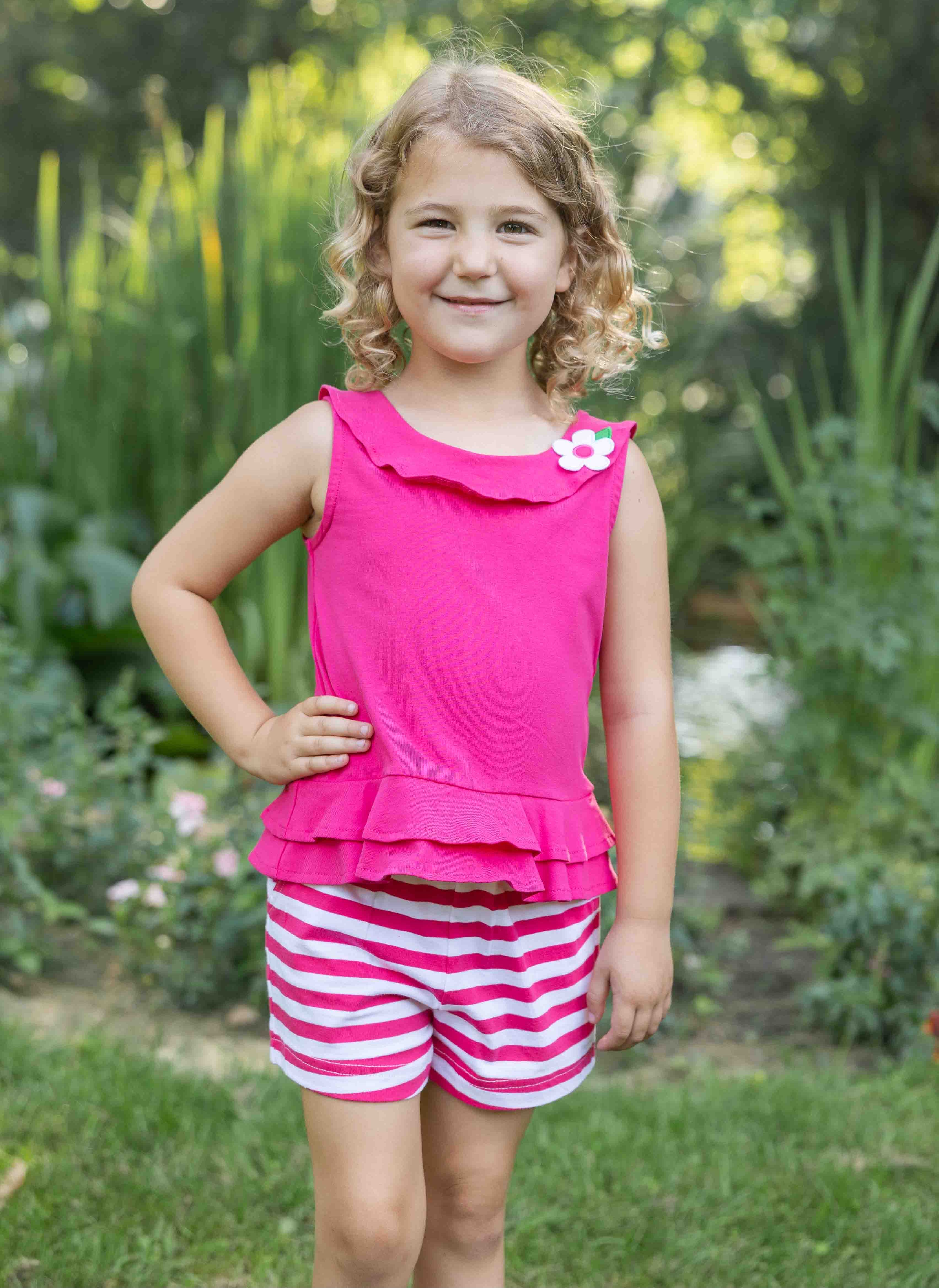Young girl in a pink top and striped shorts standing in a garden.