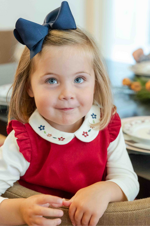 Young girl with a blue bow in her hair, wearing a red dress with a white collar.