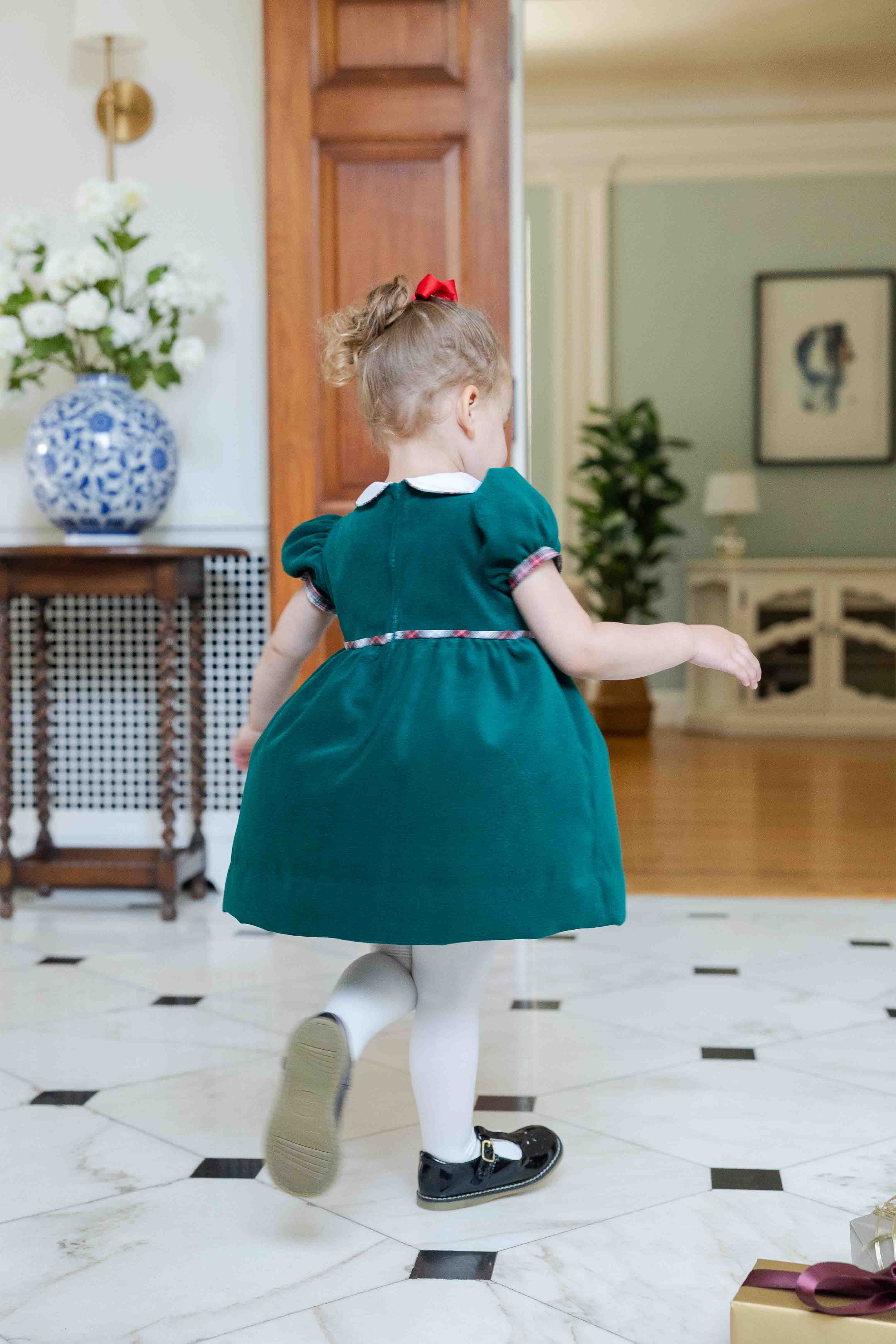 Child in a green dress walking in a room with decorative elements.