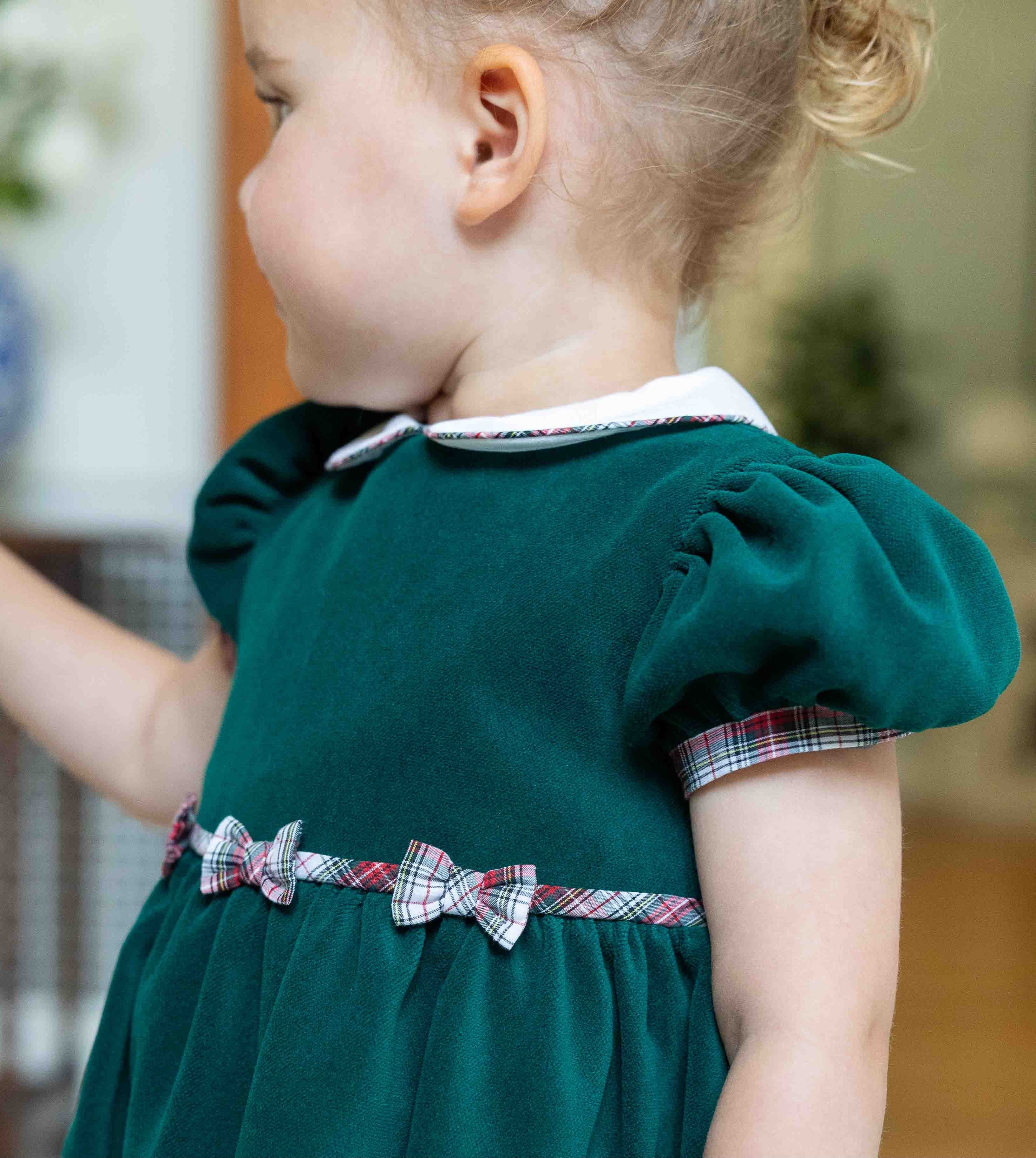 Child wearing a green dress with plaid accents in an indoor setting