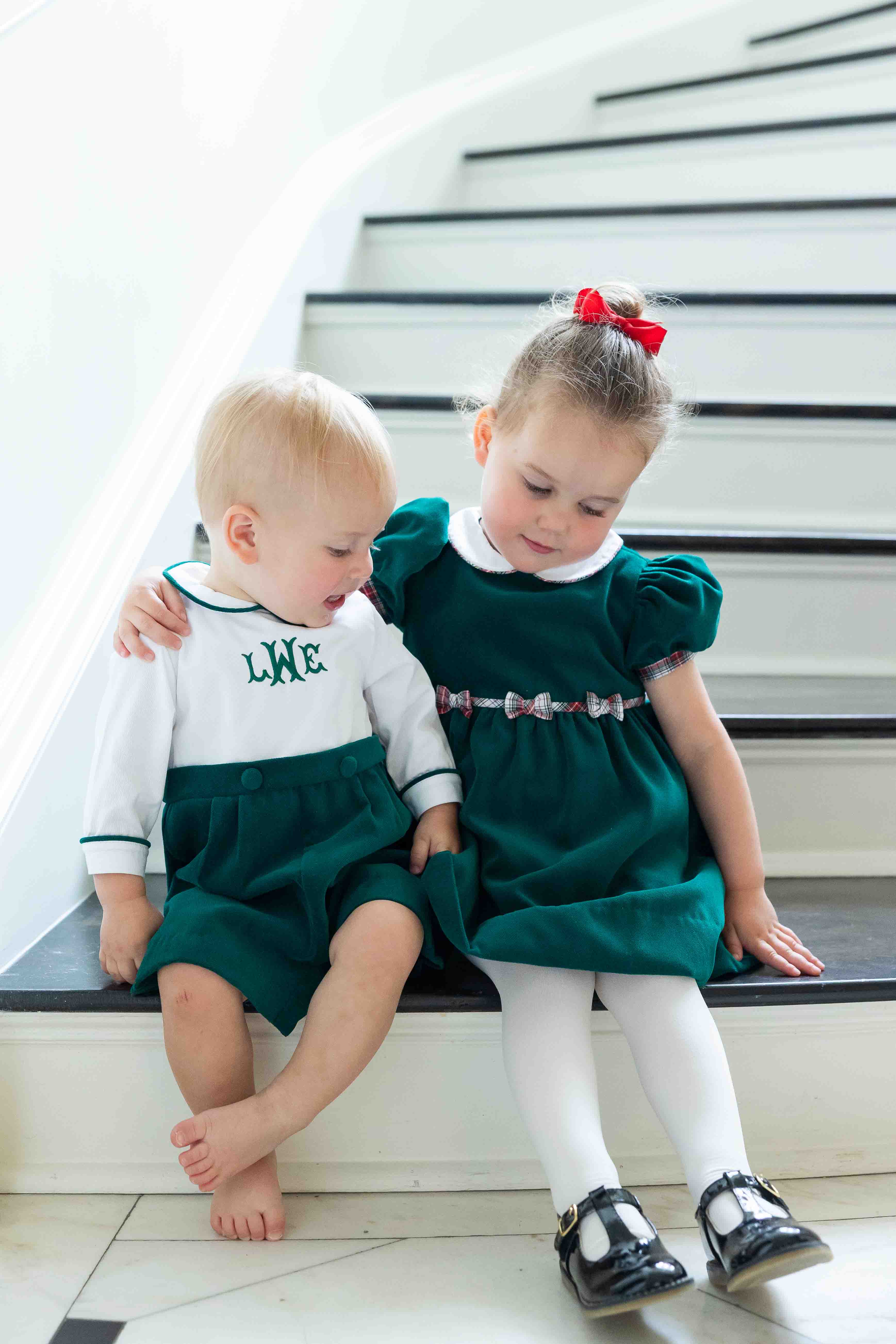 Two children in matching green outfits sitting on a staircase.