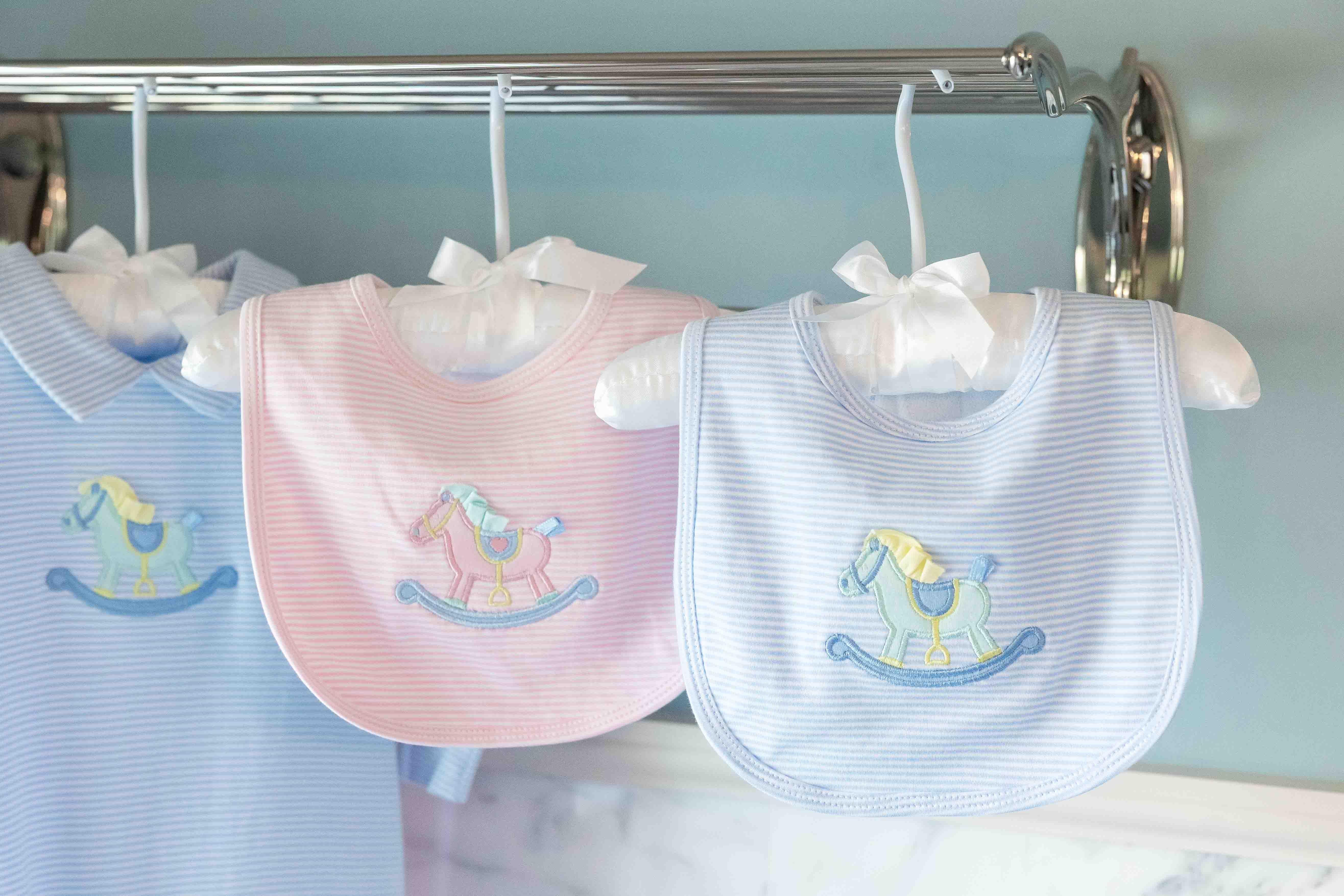 Two baby bibs with rocking horse design on a rack against a light blue wall.