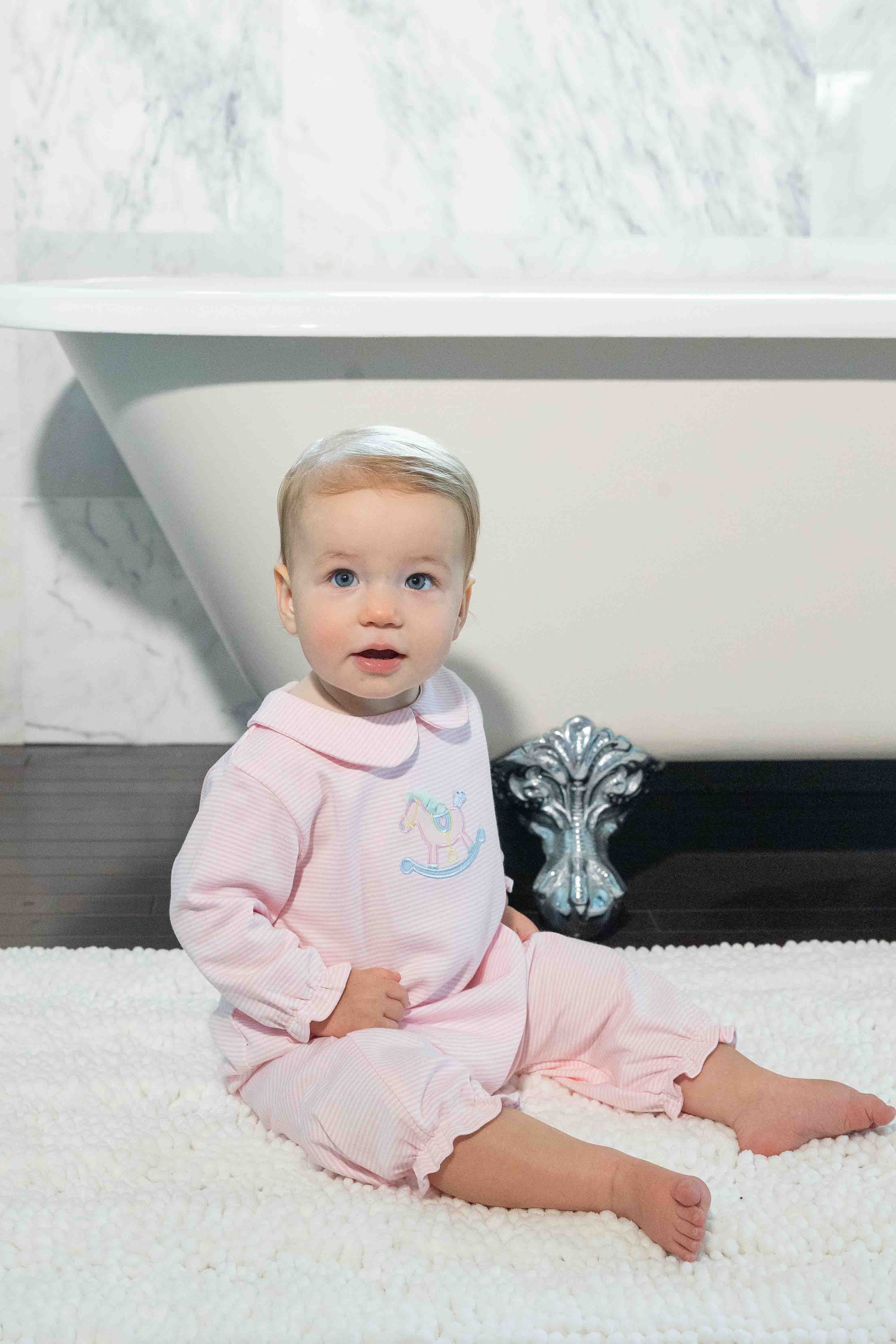 Baby in pink outfit sitting in a bathroom floor rug