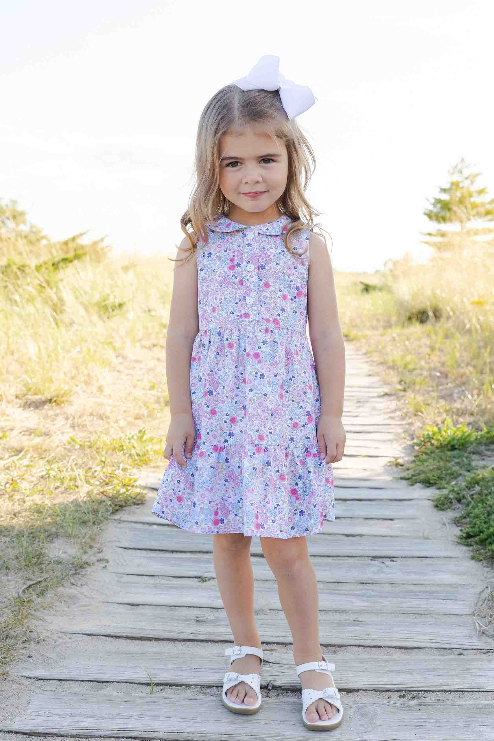 Young girl in a floral dress standing on a wooden path with a natural background