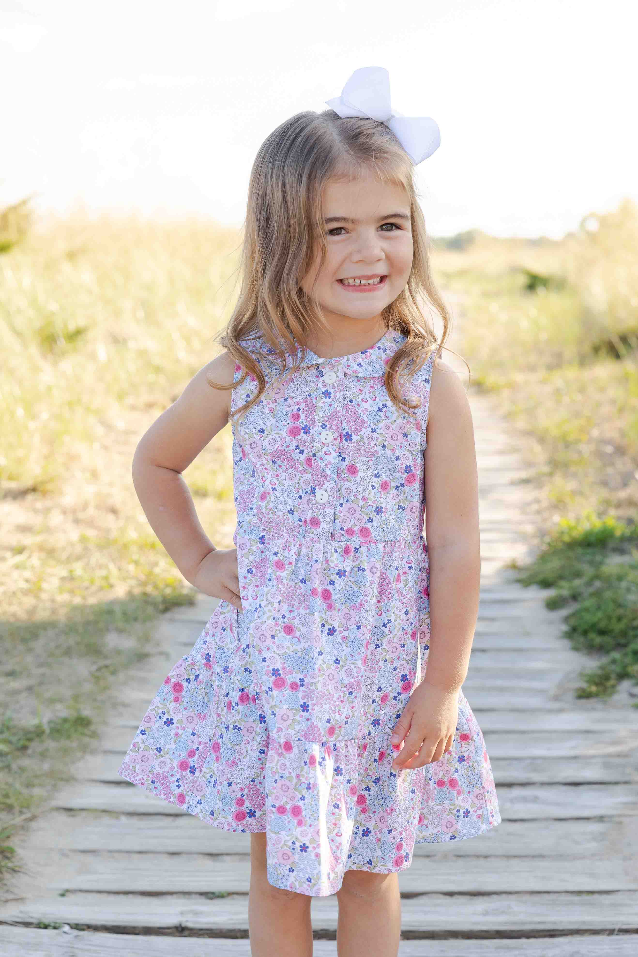 Young girl in a floral dress standing on a wooden path with grass and flowers in the background
