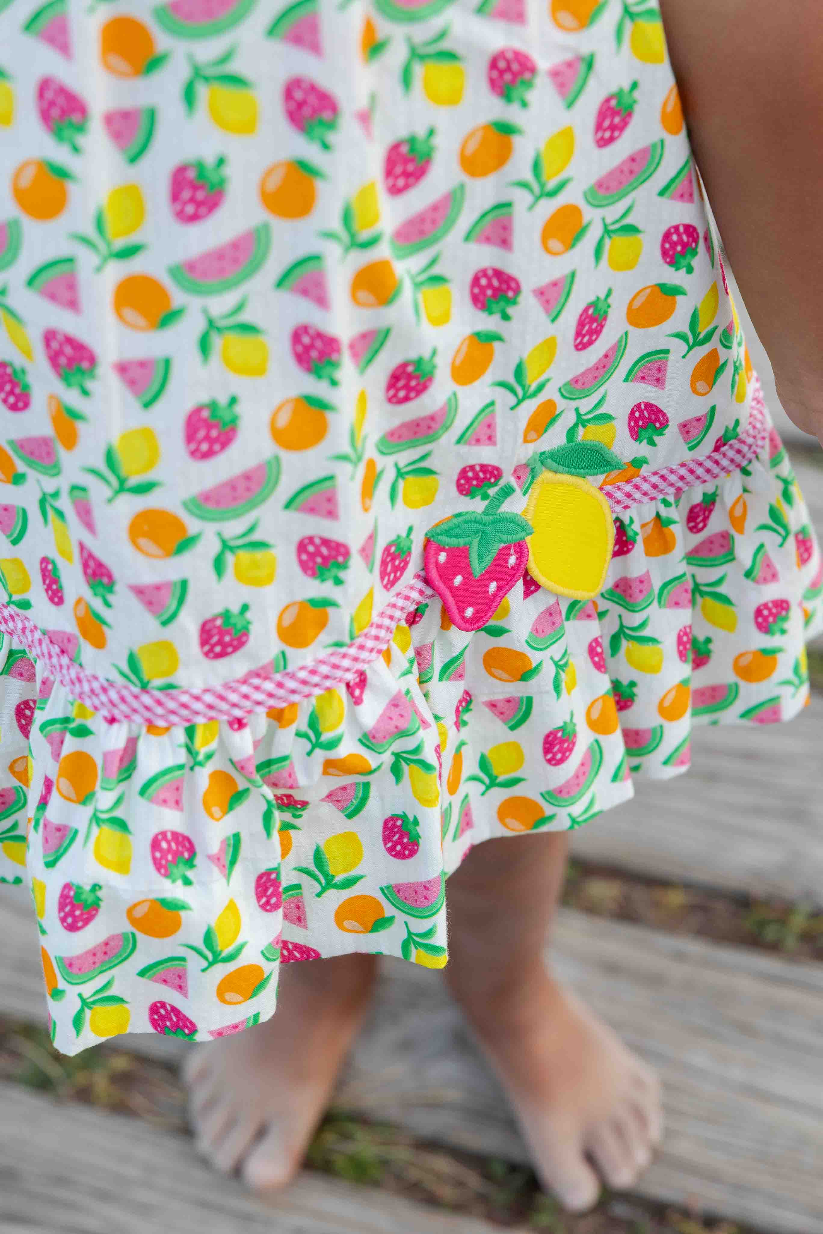 Child's dress with a colorful fruit pattern on a wooden floor.