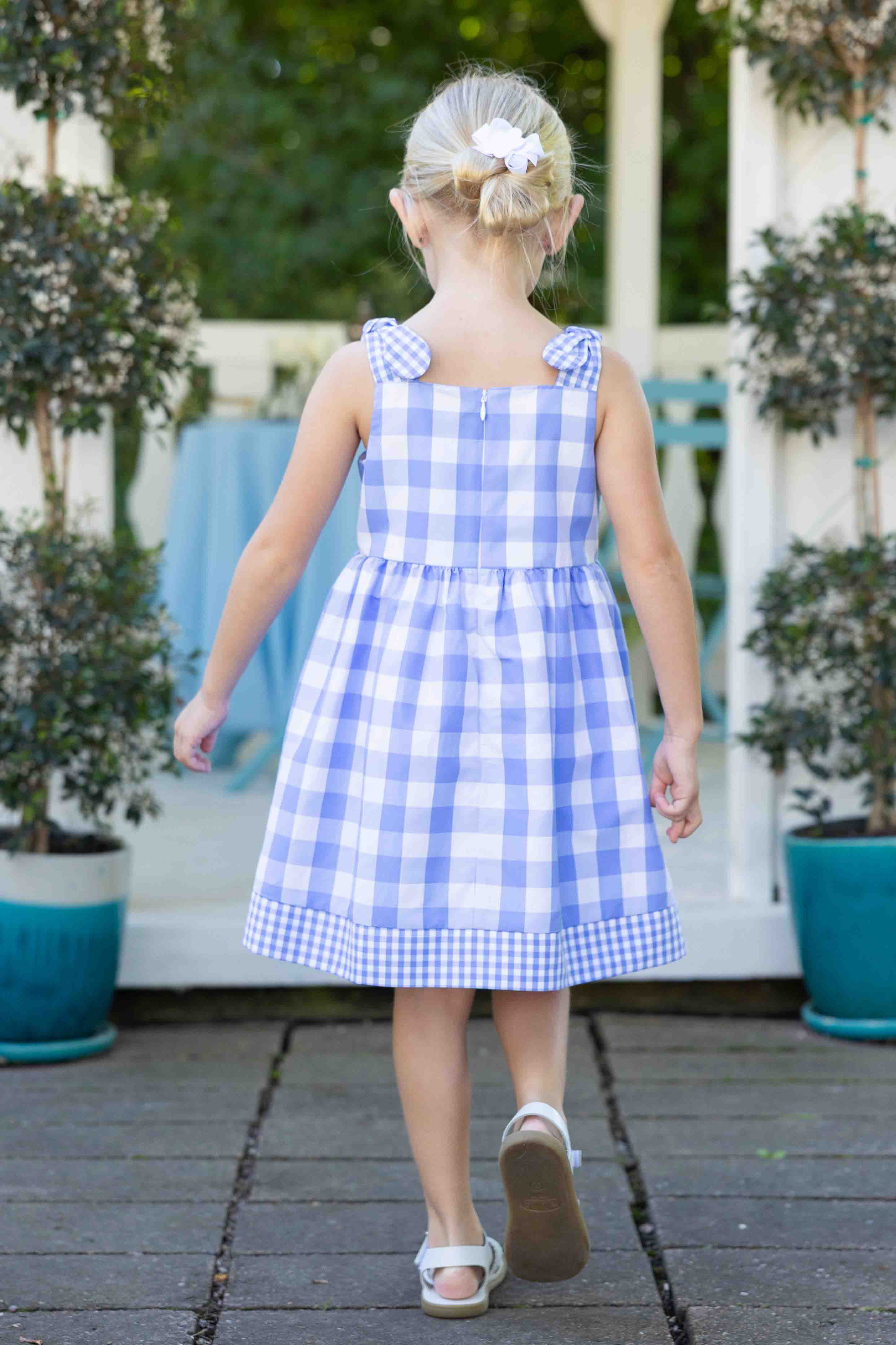 Young girl wearing a blue and white checkered dress outdoors.