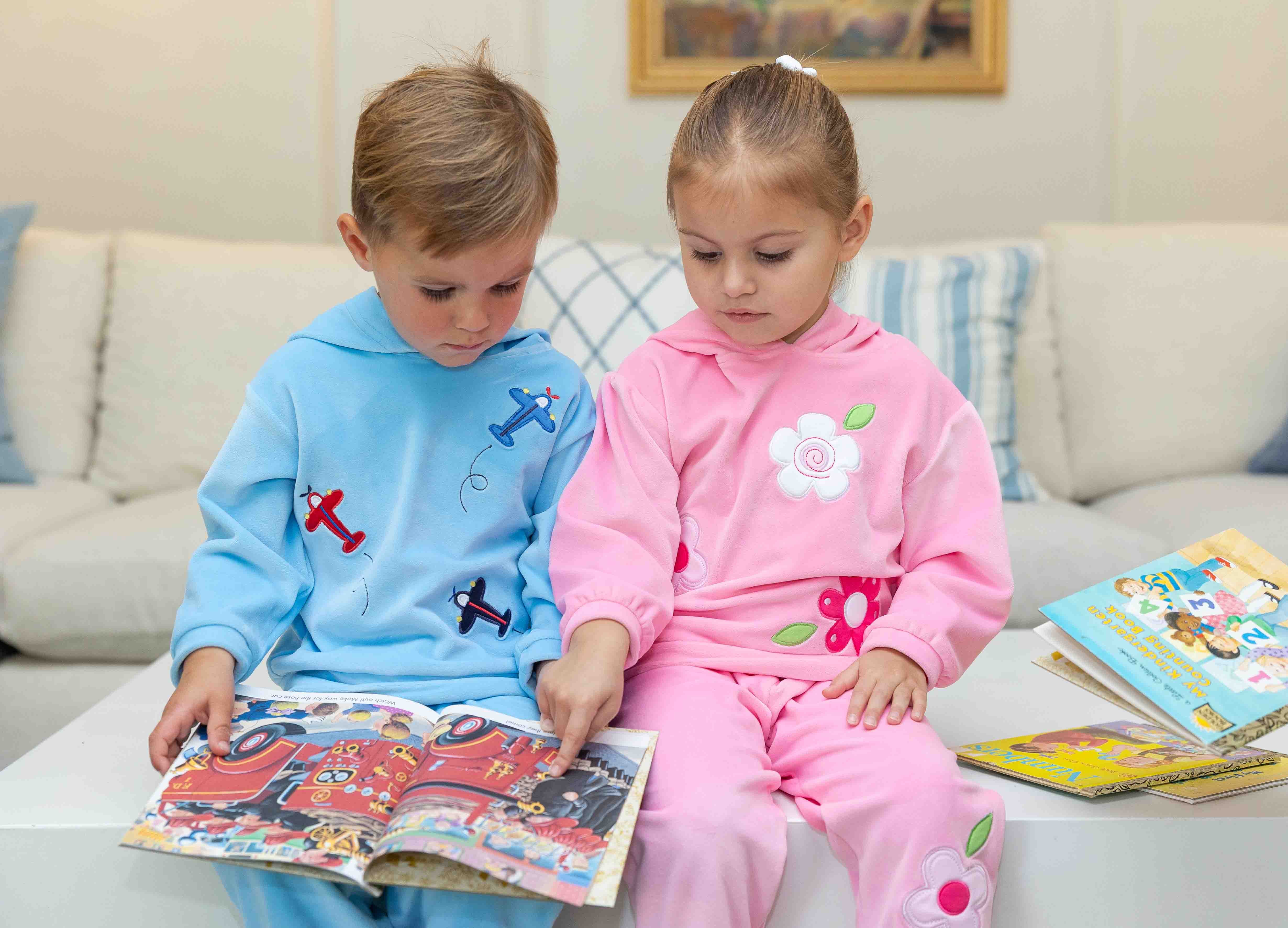 Two children in pajamas sitting on a couch reading books.
