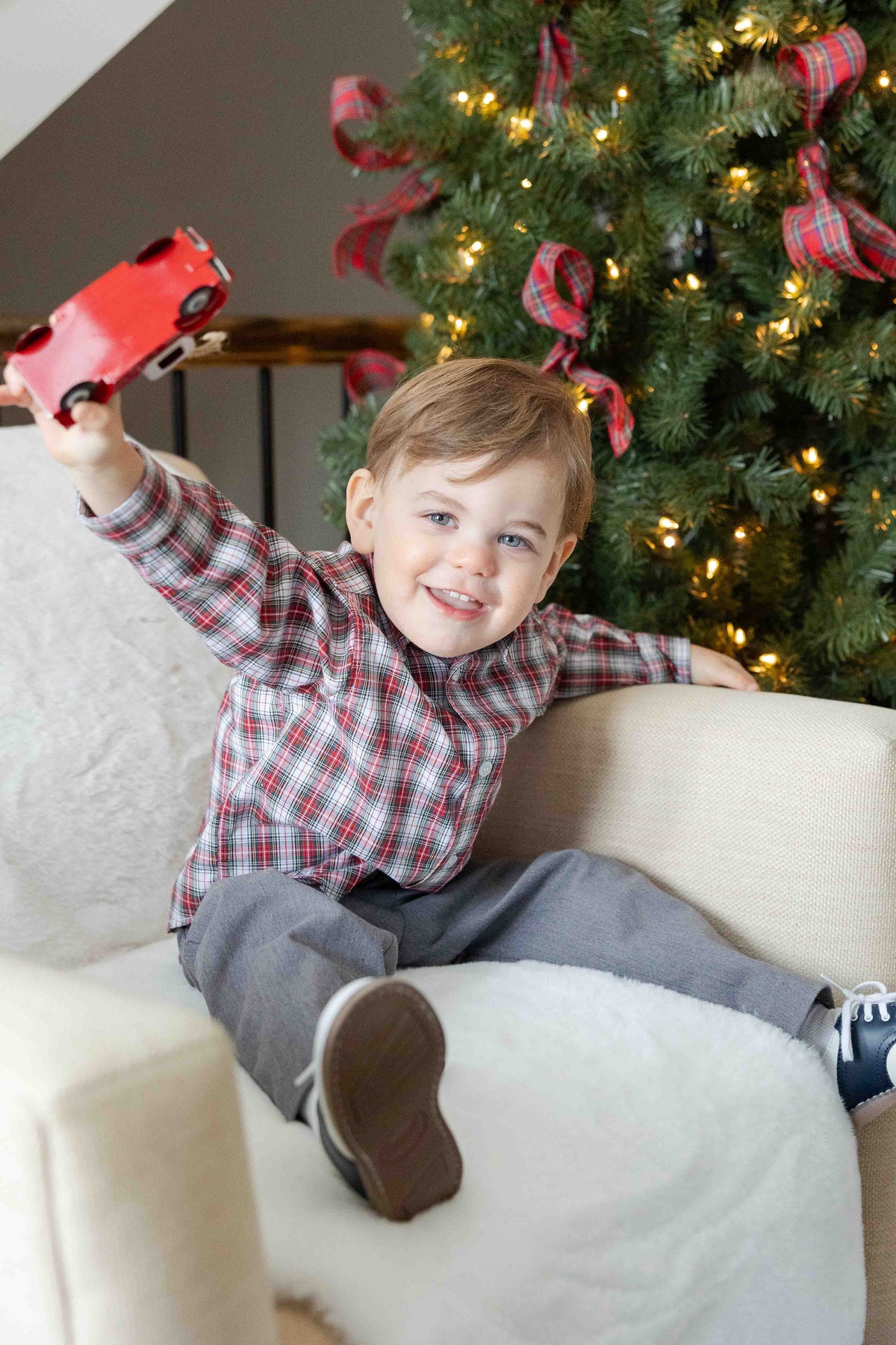 Child holding a red toy car in front of a decorated Christmas tree.