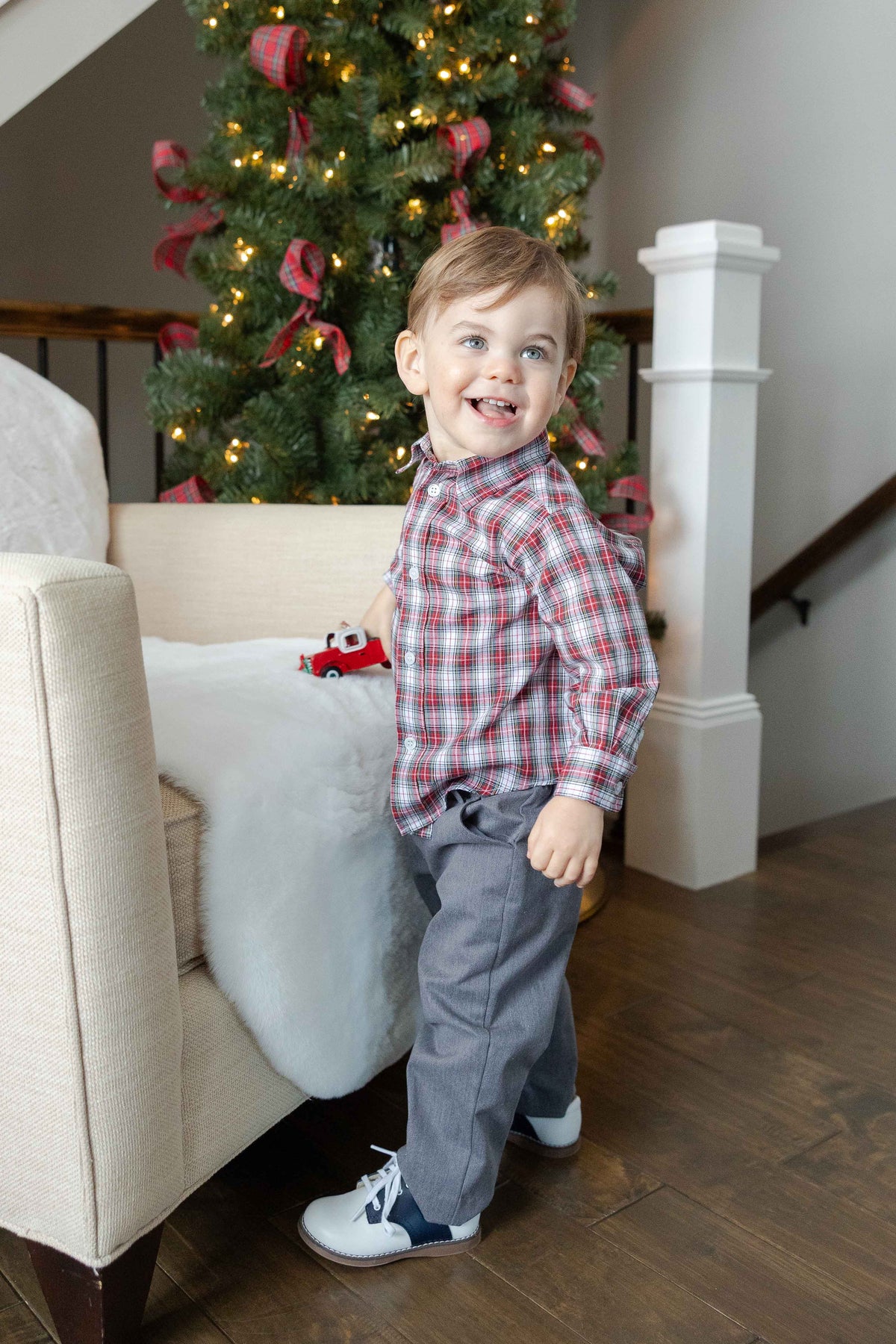 Child standing in a living room with a decorated Christmas tree in the background