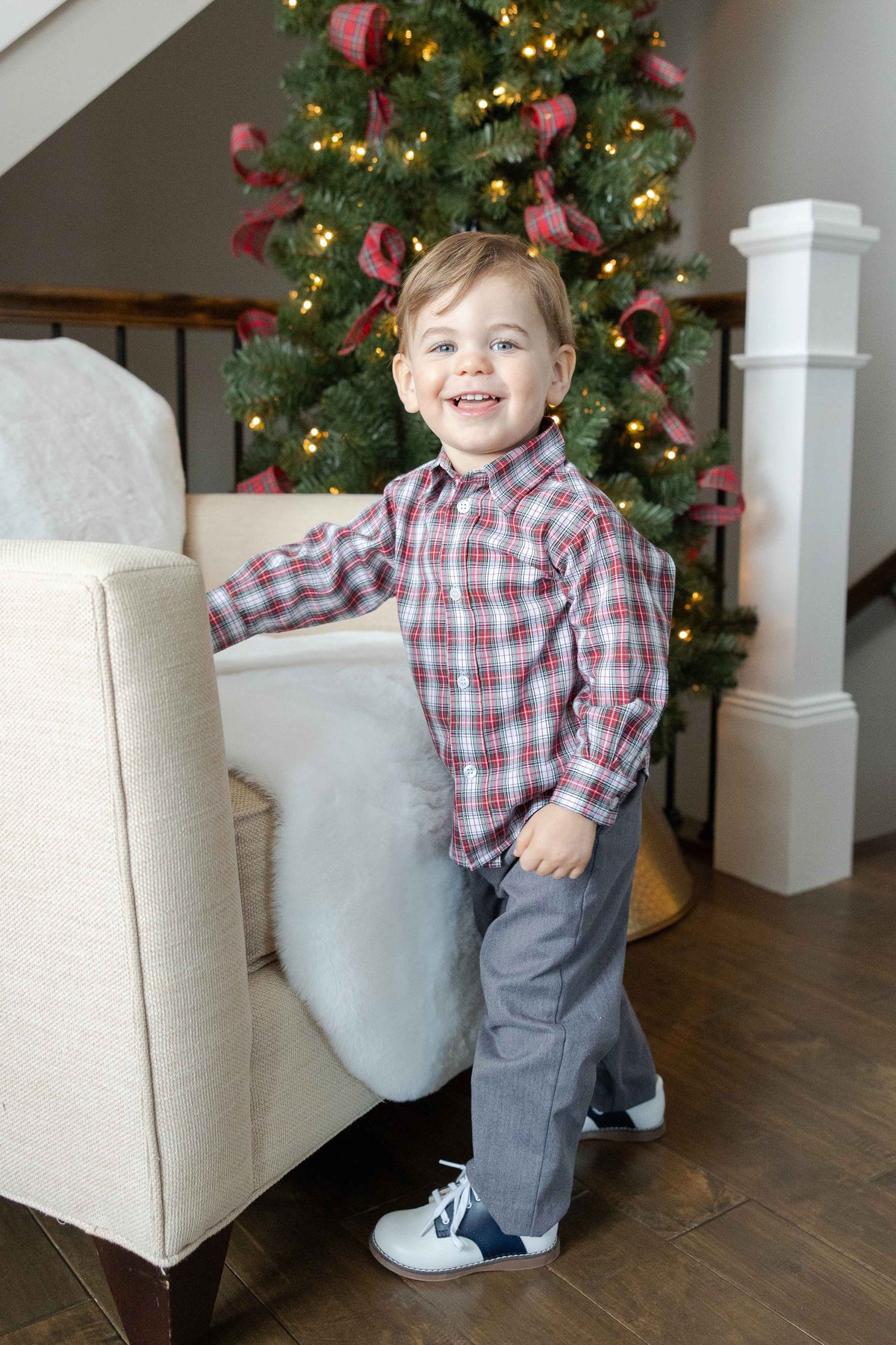 Child in a plaid shirt standing in front of a decorated Christmas tree.