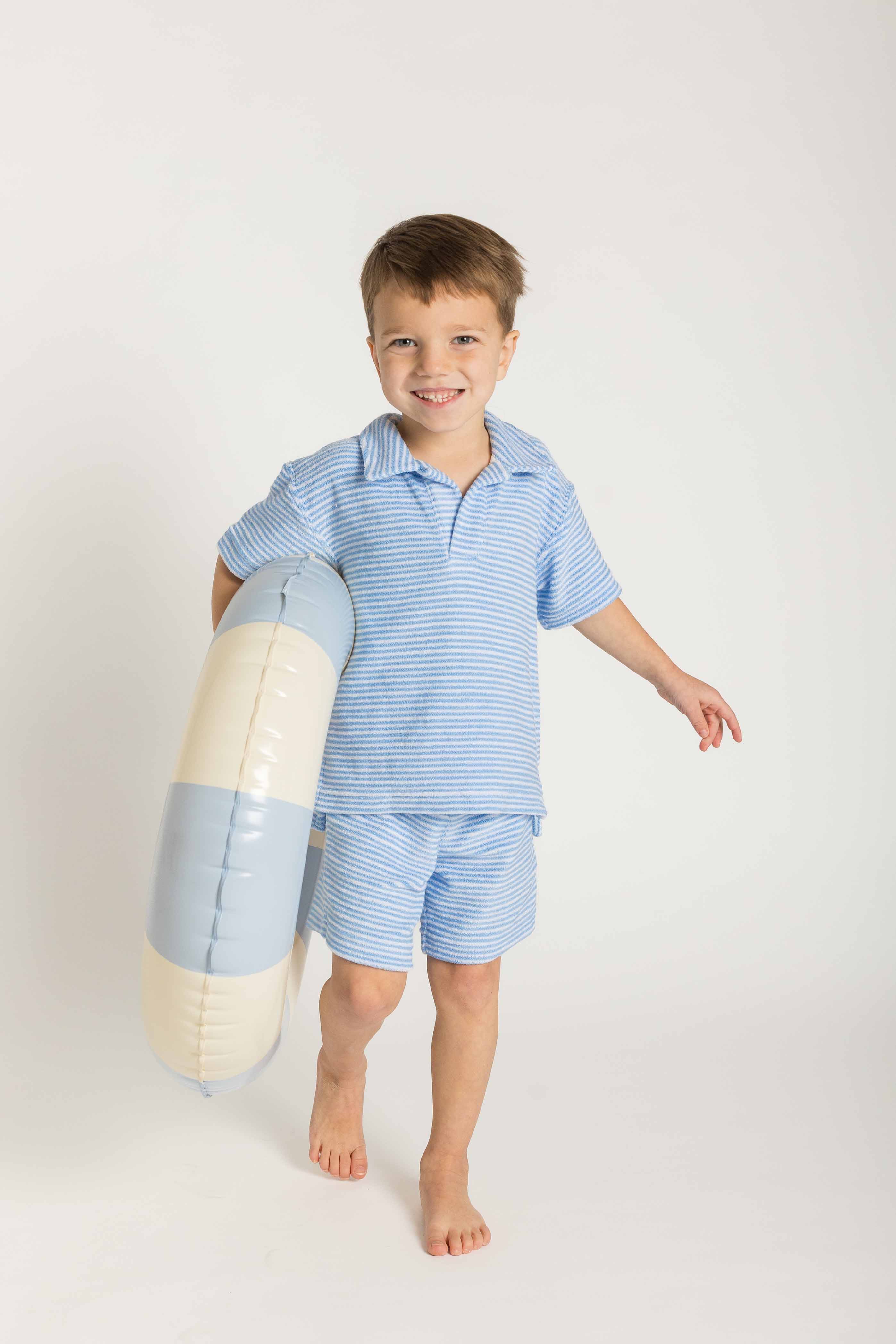 Child wearing a blue striped shirt and shorts holding a stripe floatie on a white background