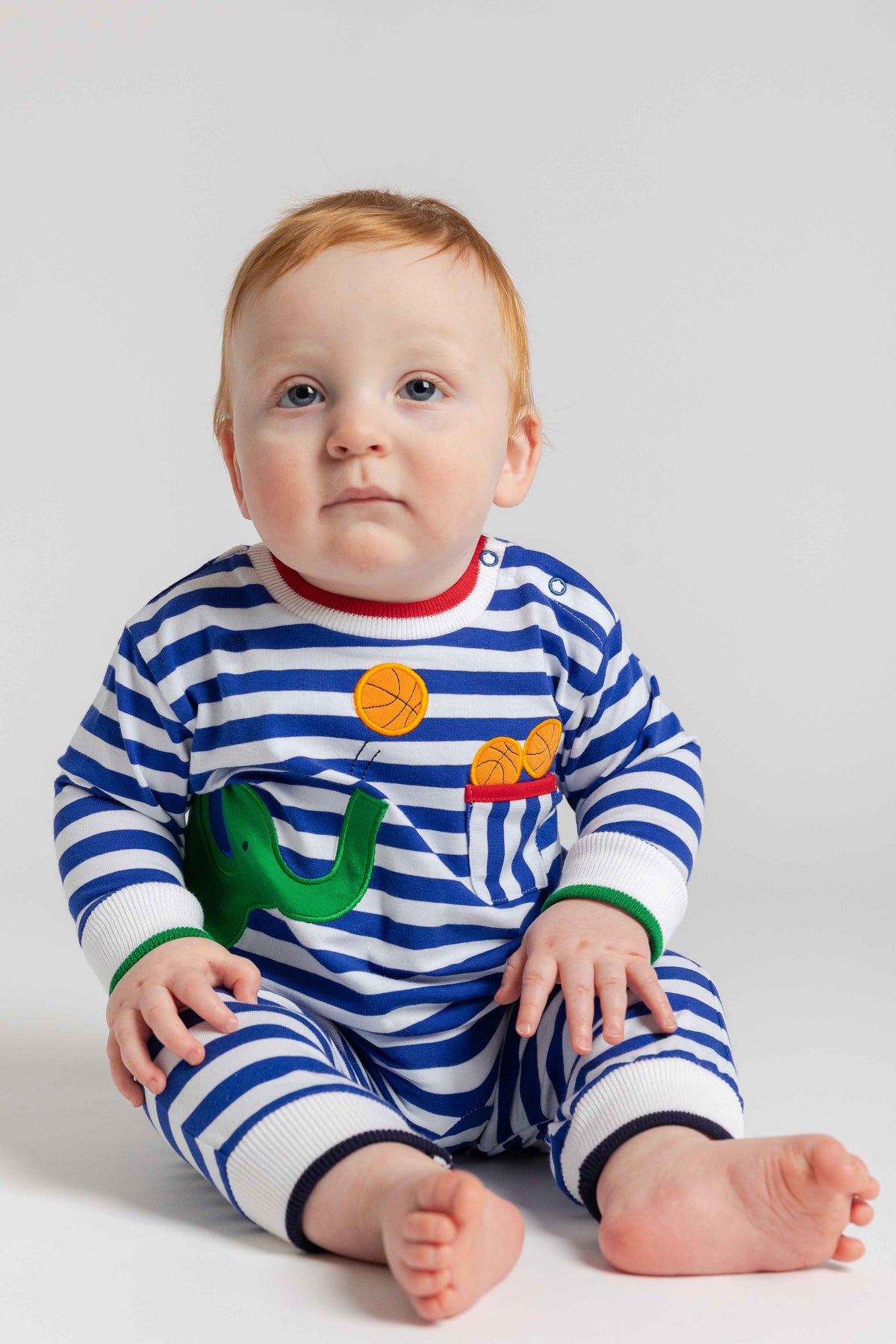 Baby wearing a blue and white striped outfit with colorful accents on a plain background