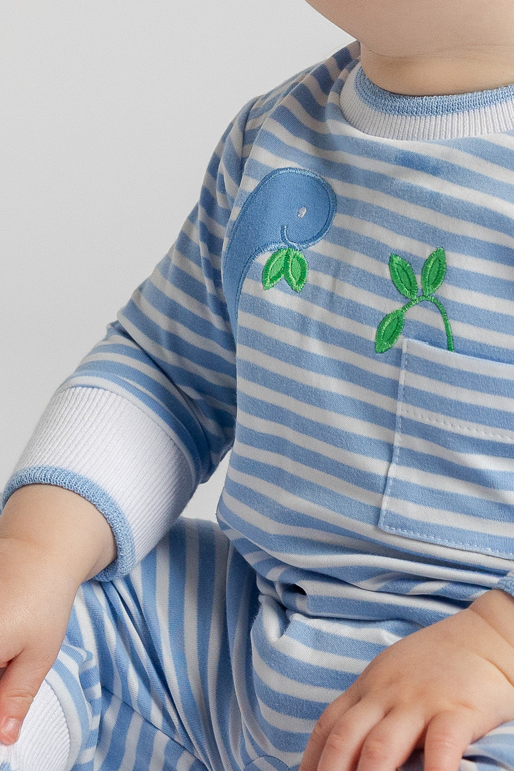 Close-up of a child wearing a blue and white striped outfit with embroidered designs on a plain background