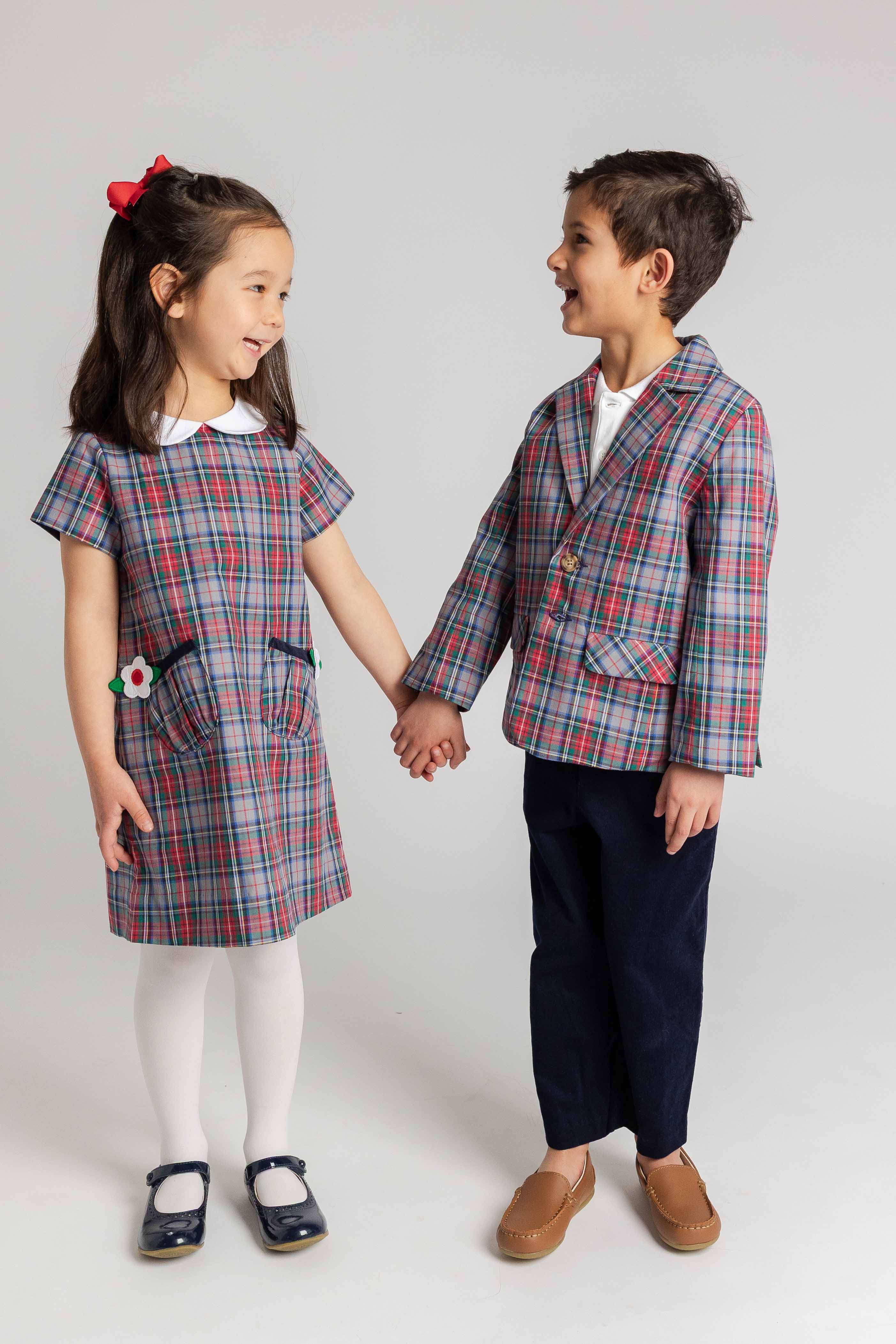 Two children in matching plaid outfits standing against a white background
