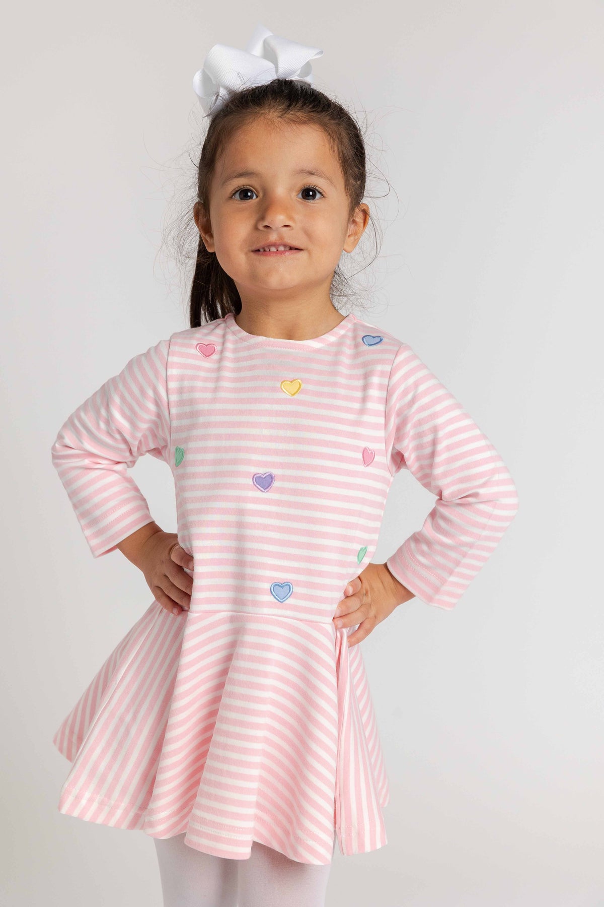 Young girl wearing a pink and white striped dress with heart patterns on a plain background