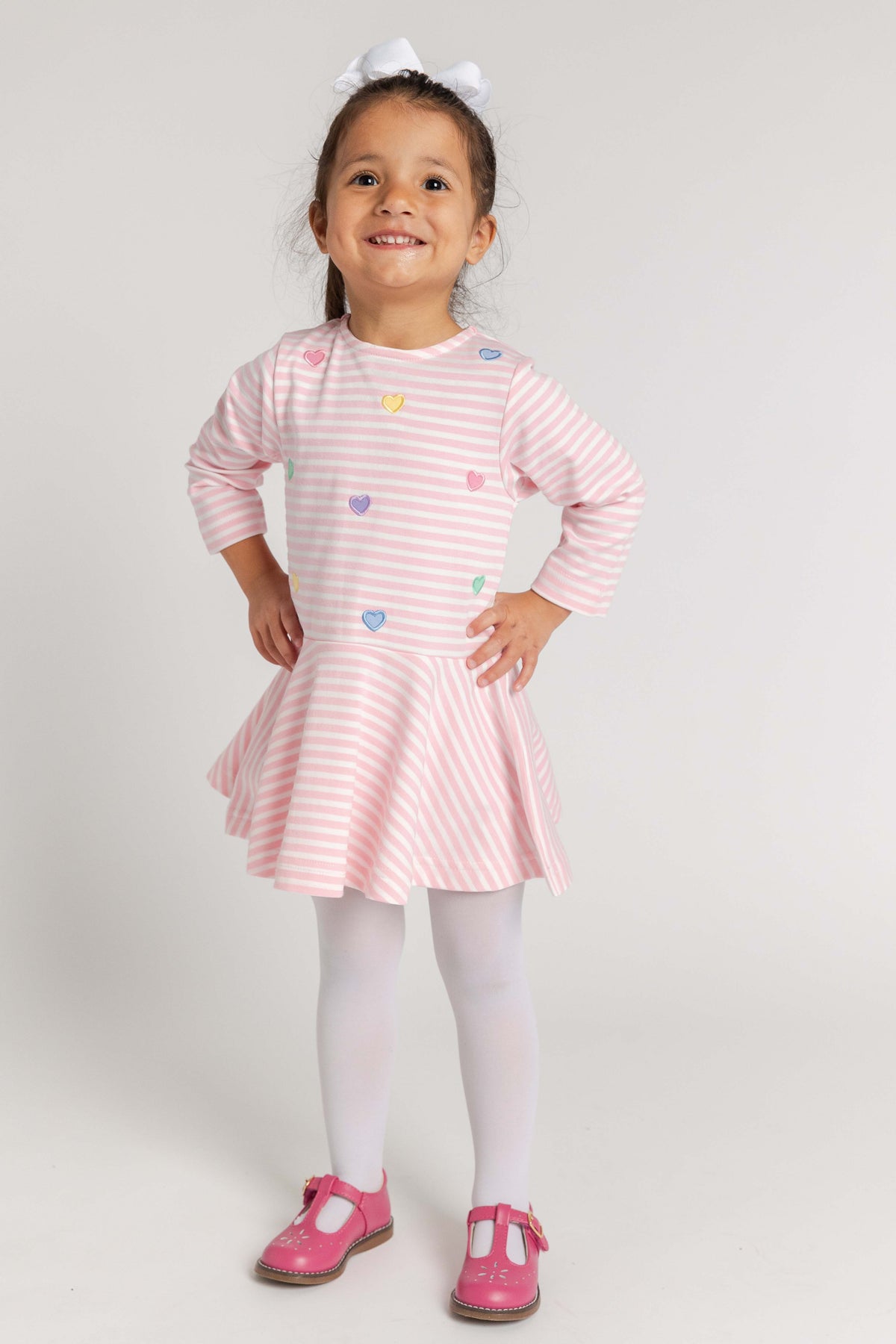 Young girl wearing a pink striped dress with colorful buttons on a white background
