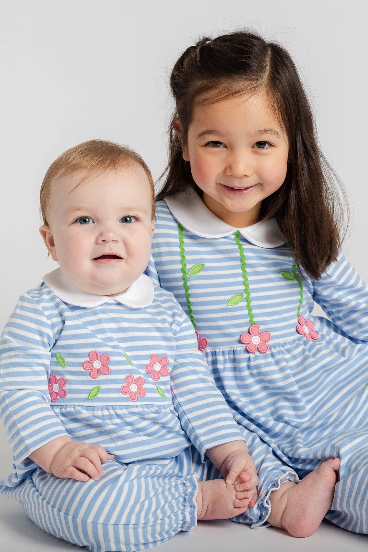 Two children wearing matching blue and white striped outfits with floral designs on a light gray background.