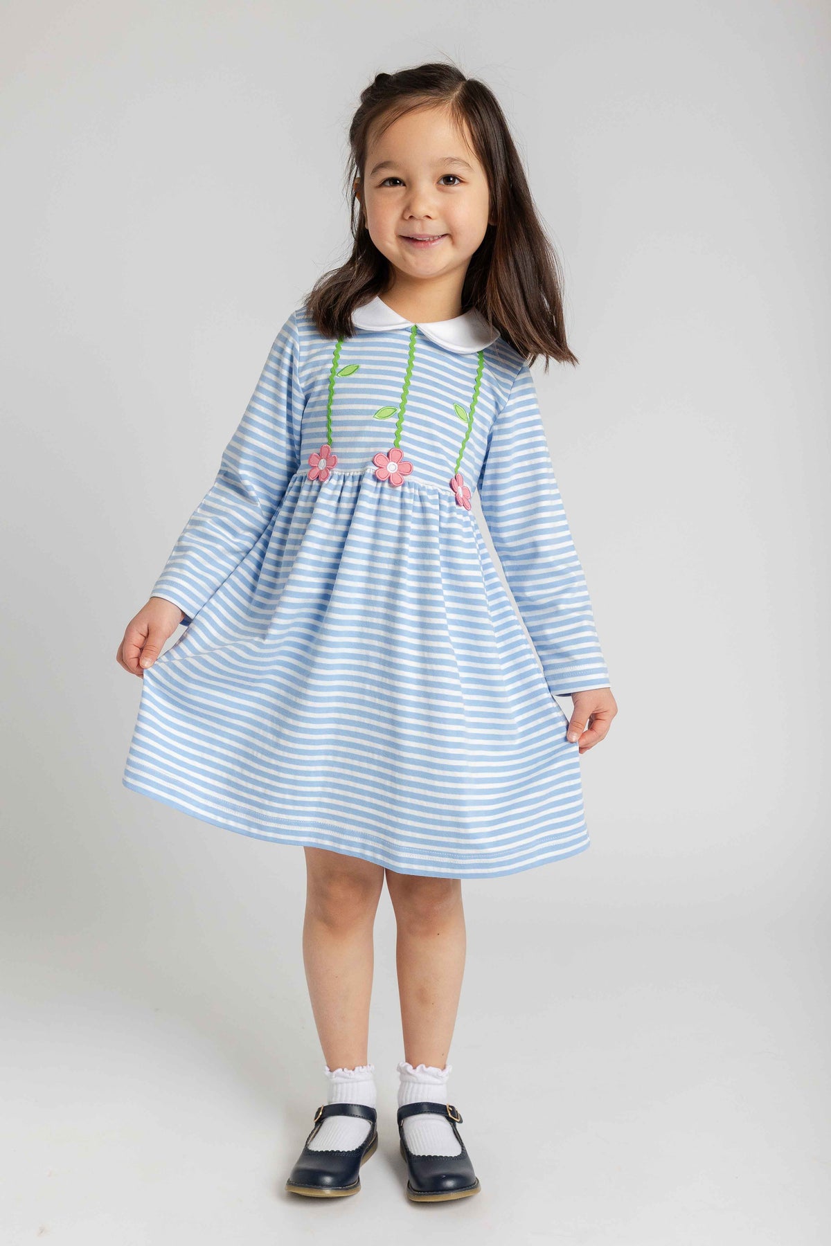 Young girl wearing a blue and white striped dress with floral details on a plain background