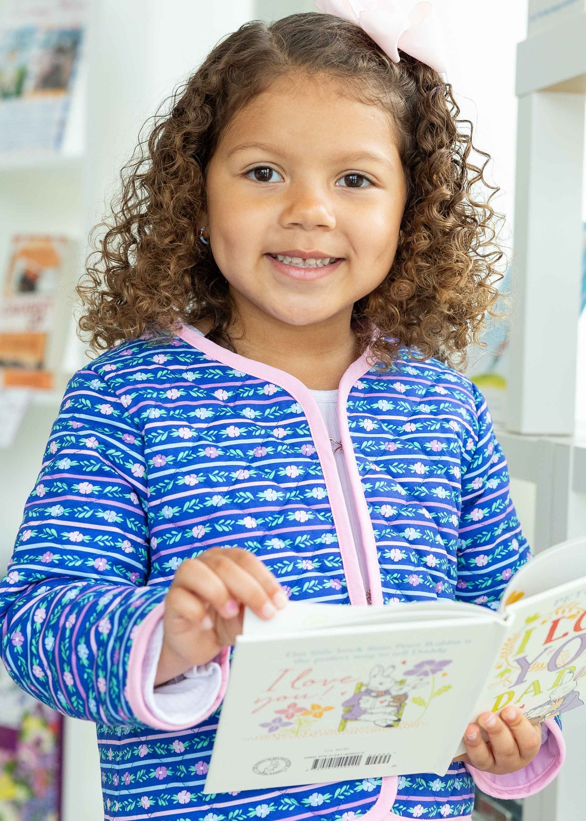 Child wearing a blue and white patterned outfit holding a book indoors.