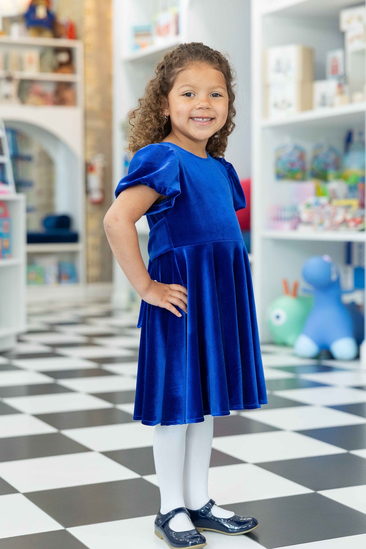Young girl in a blue dress standing in a store with shelves in the background