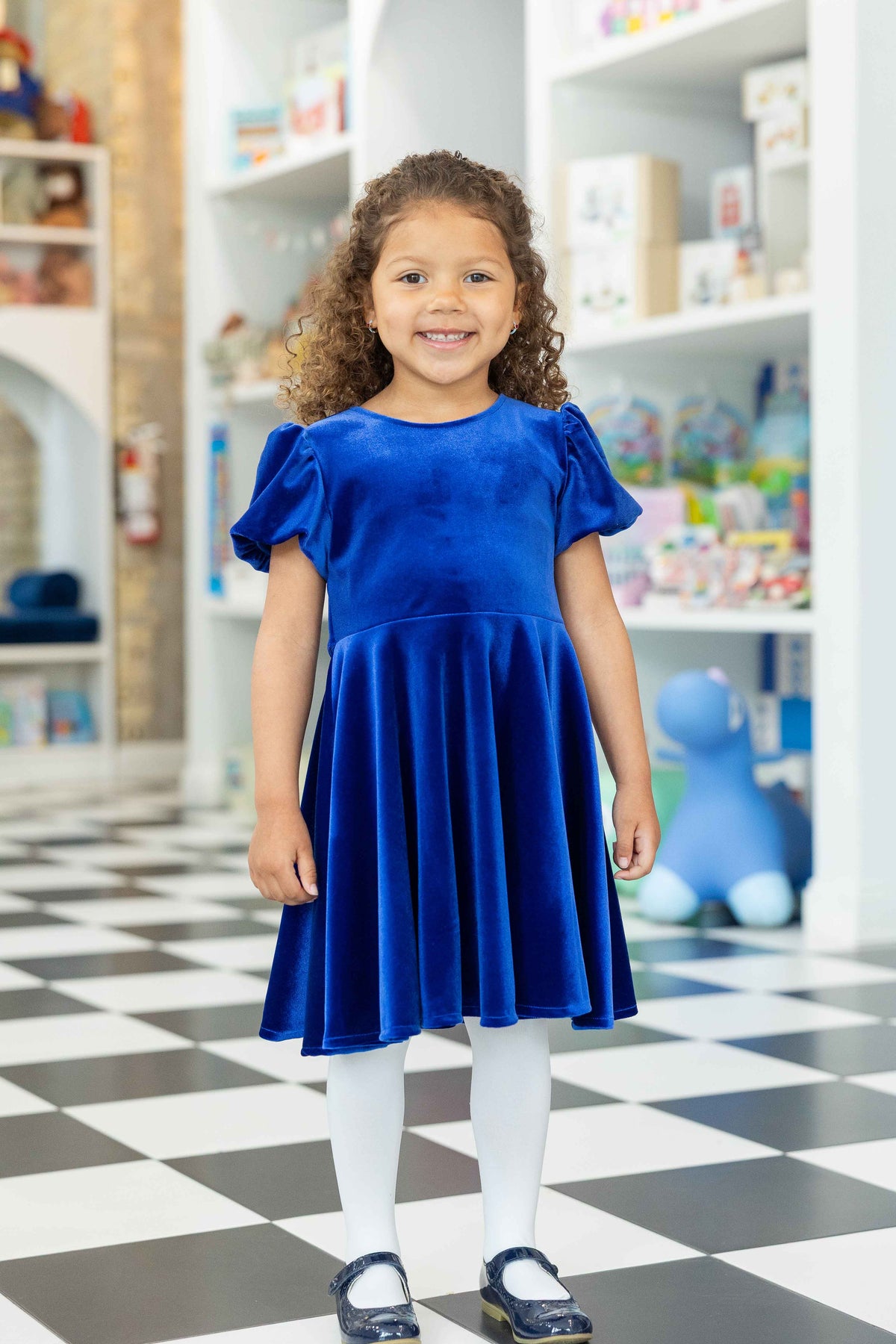 Child wearing a blue dress standing in a store with shelves in the background