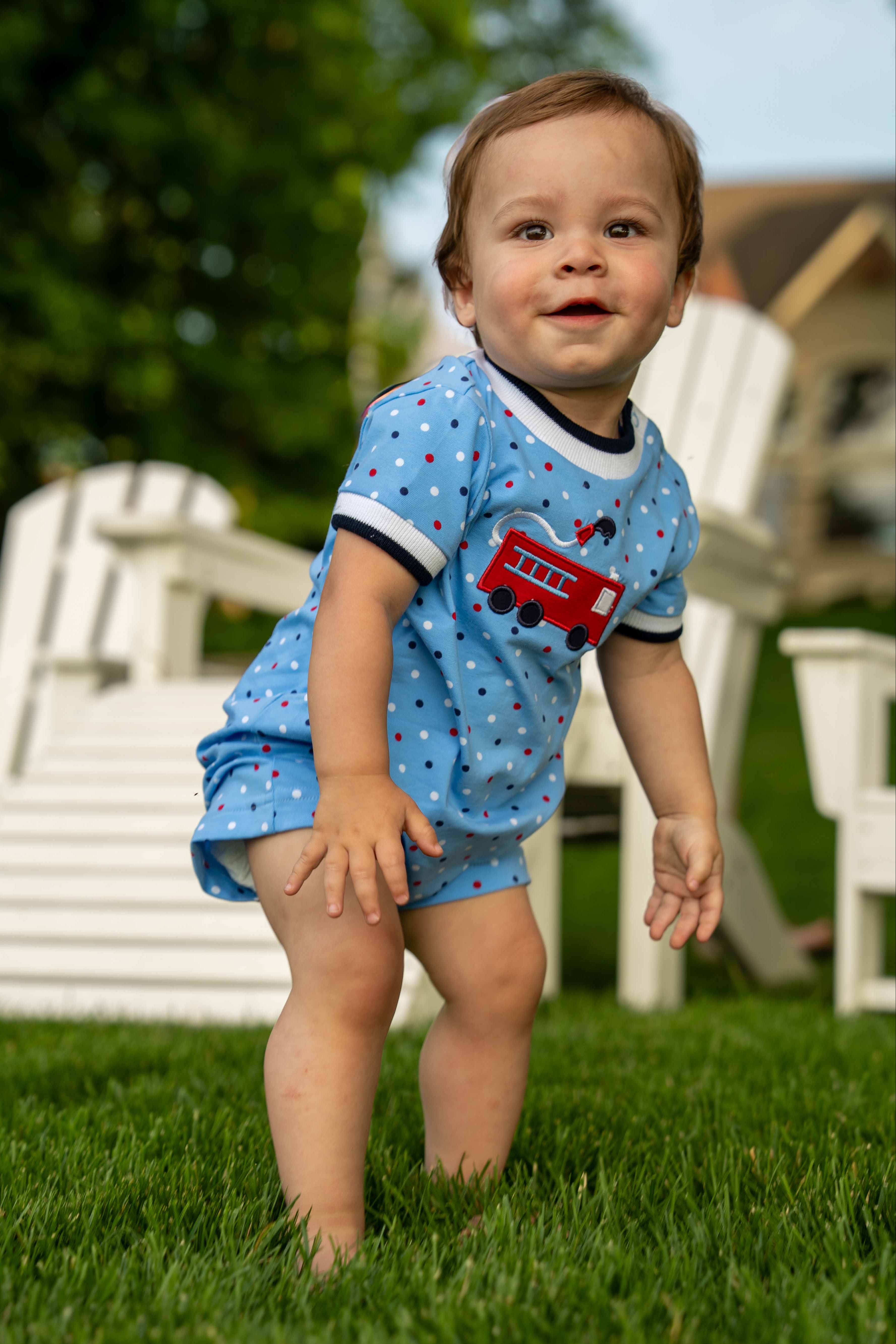 Child wearing a blue outfit with a fire truck design outdoors on grass