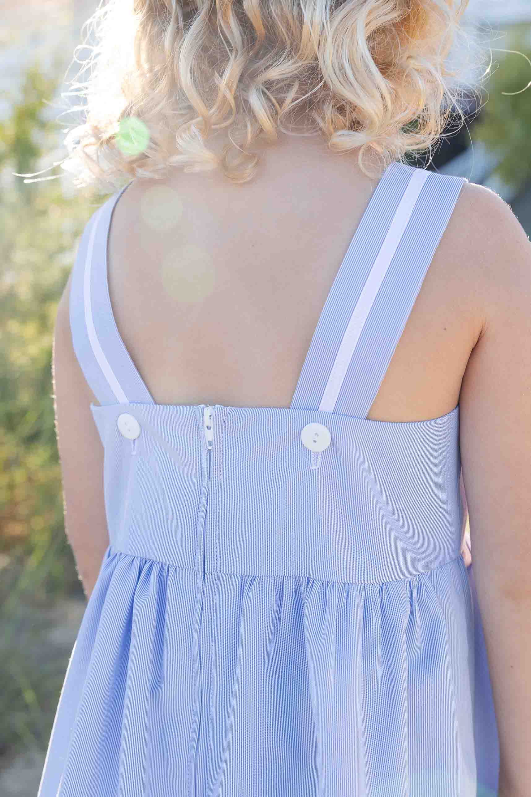 Light blue dress with white button straps on a blurred natural background