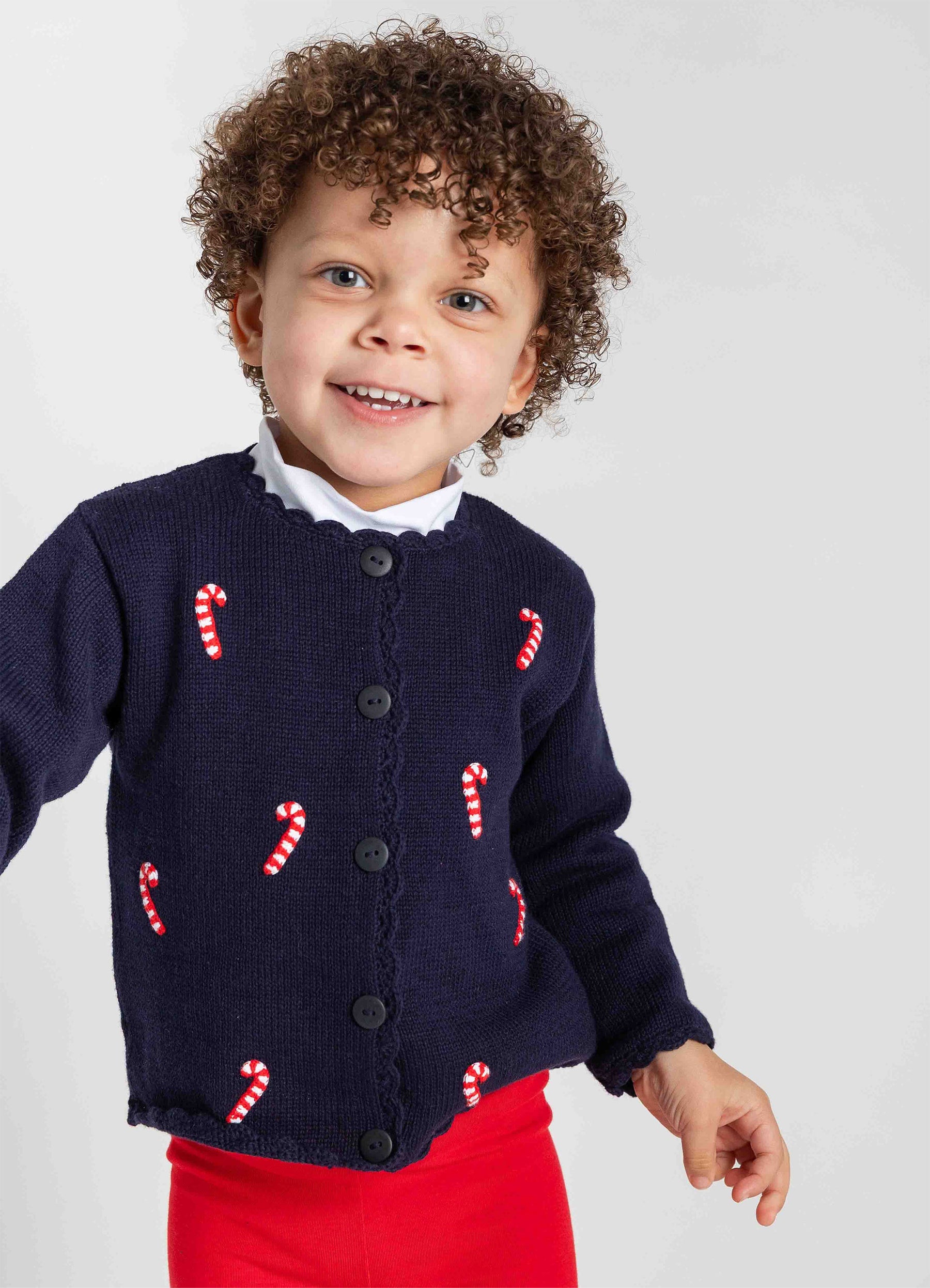 Child wearing a navy cardigan with candy cane patterns on a white background