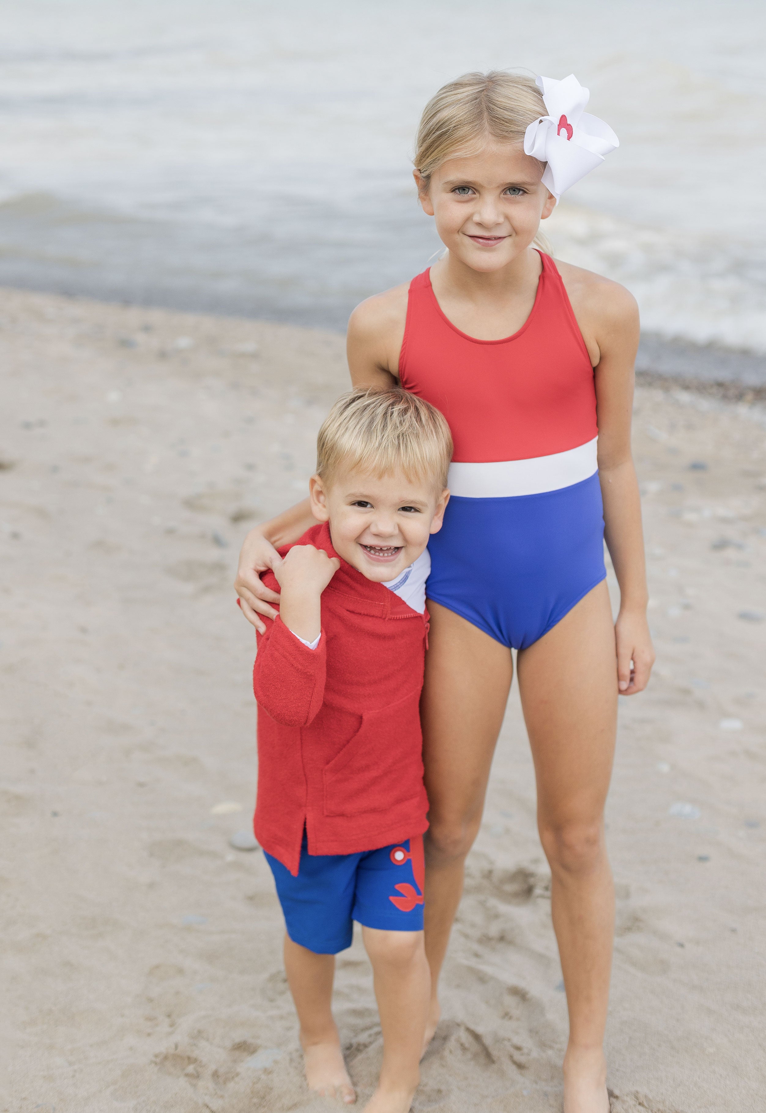young girl with younger brother in swim wear on the beach